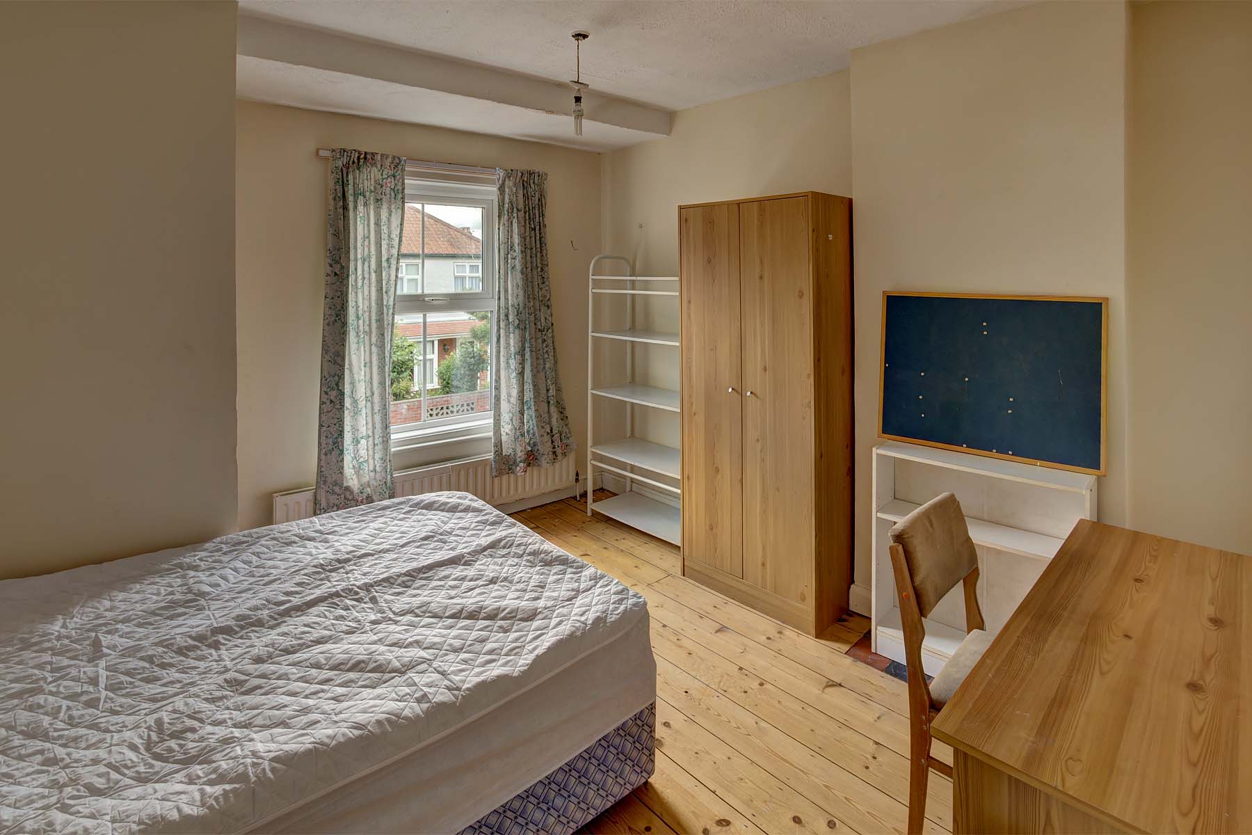 Double bedroom with wooden flooring, a divan bed base and mattress, a wooden wardrobe, desk and chair and a white TV unit.