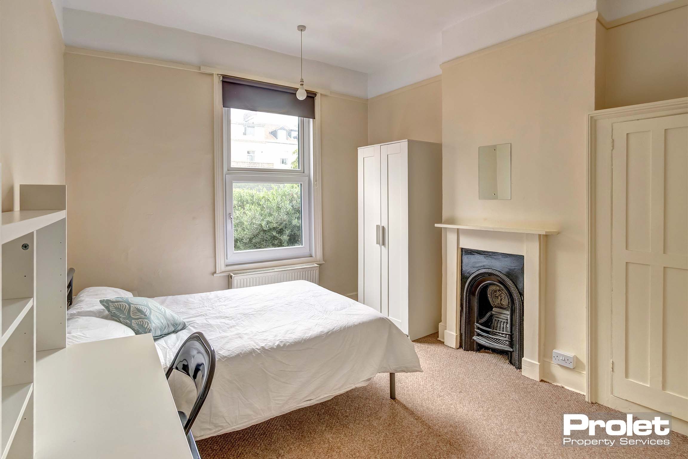 Magnolia painted double bedroom with white wardrobe and desk and a decorative fireplace.