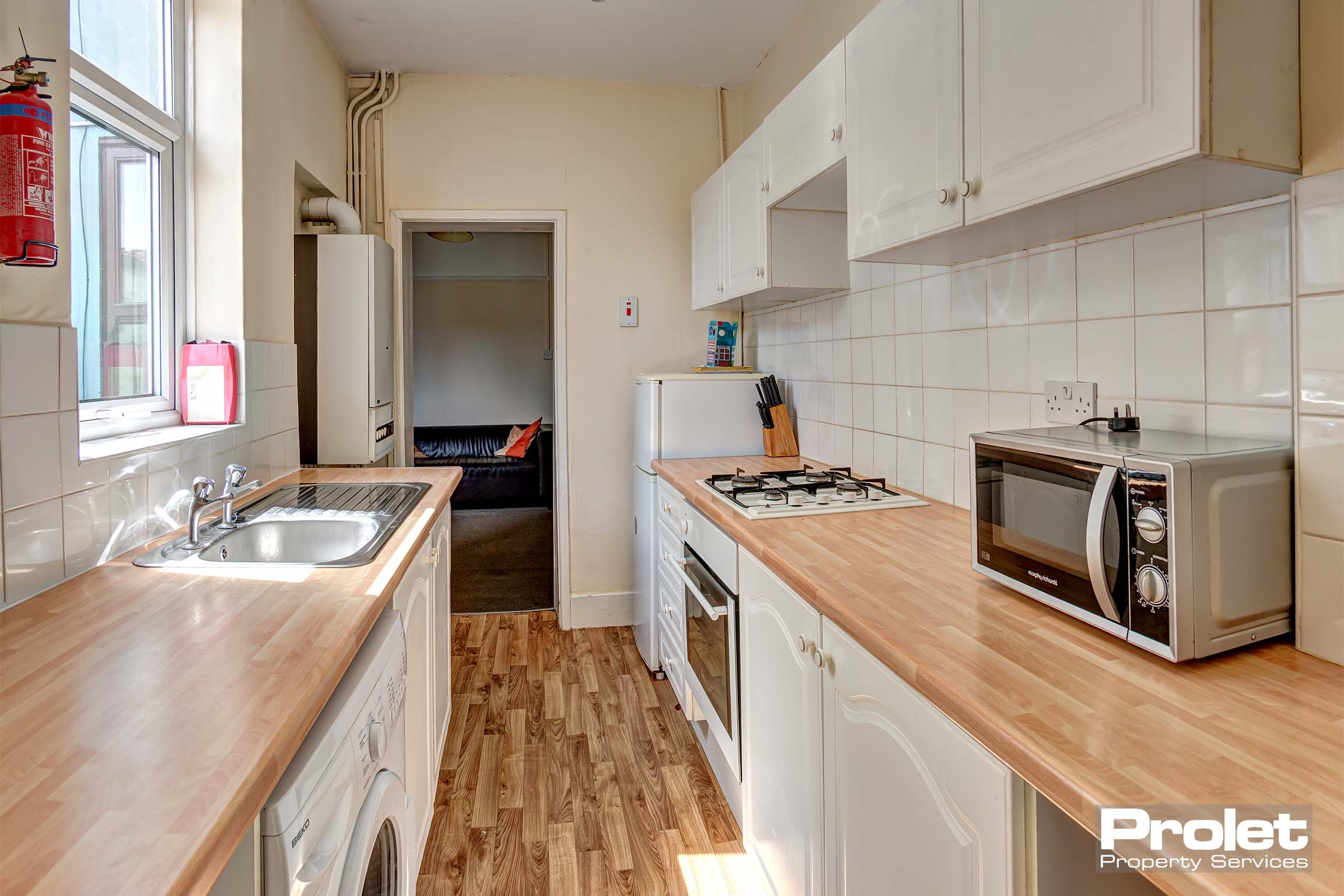 Modern galley kitchen with white cabinets and wood effect work top, and white goods.