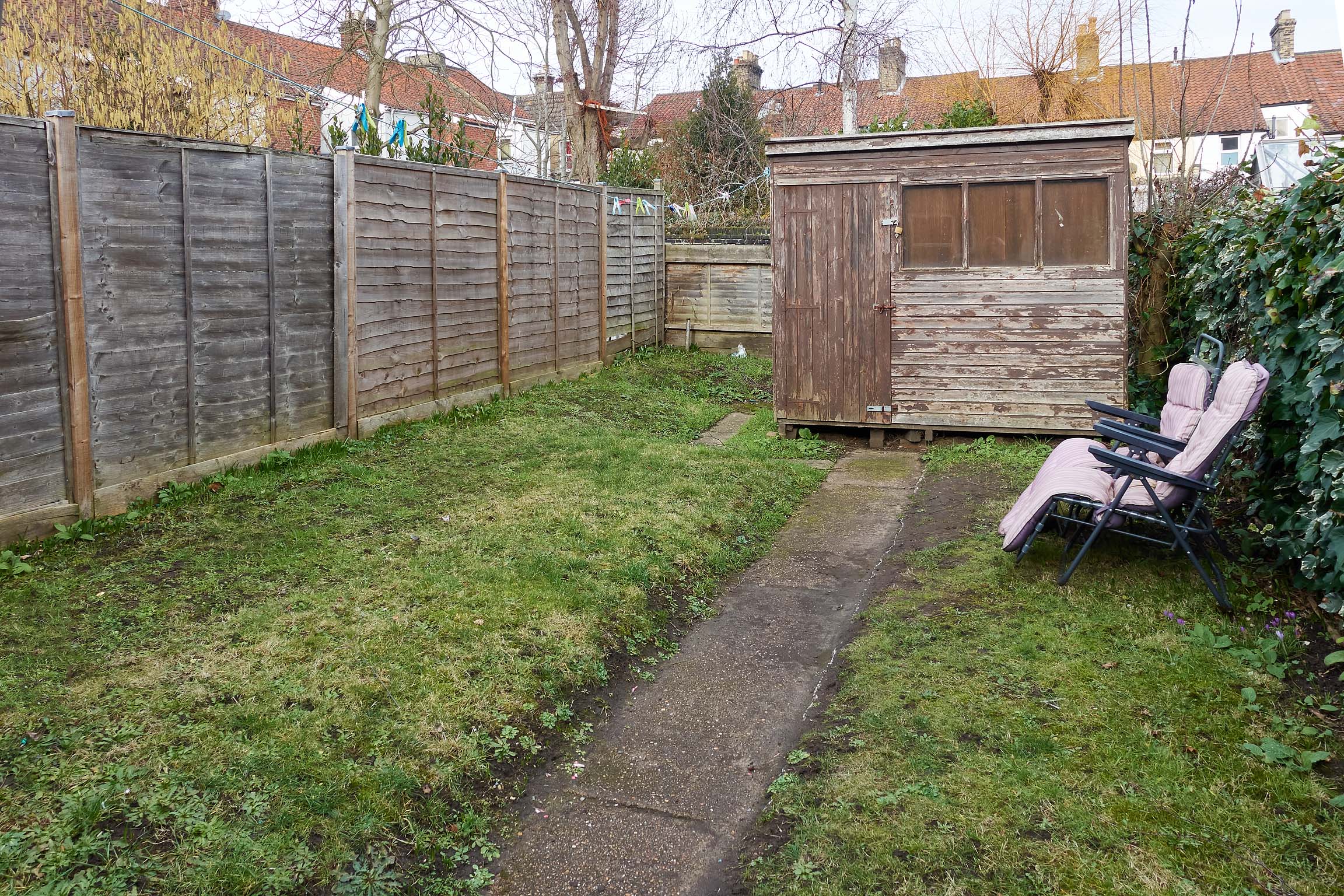 Rear garden area with grass and concrete path leading to the wooden shed.