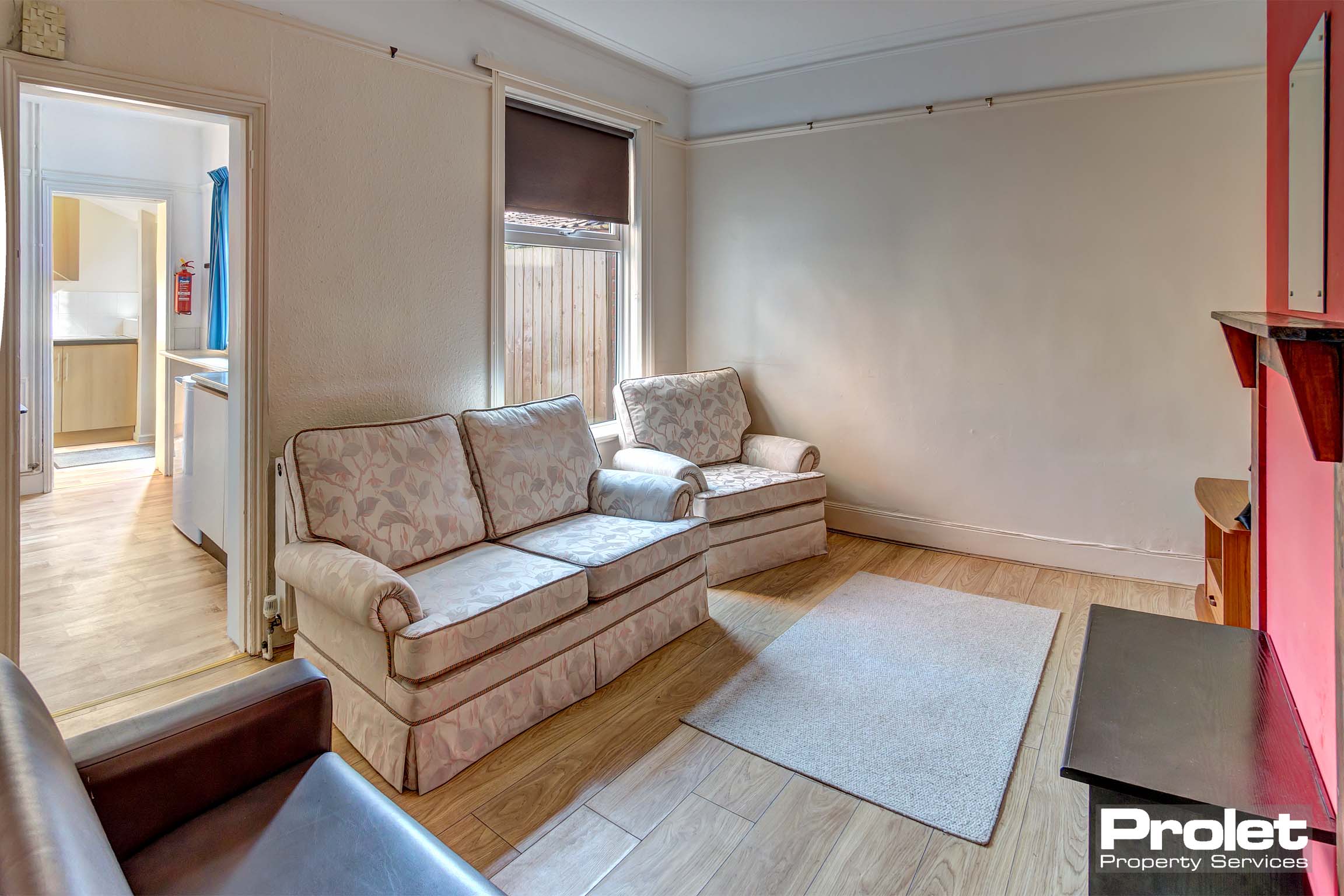 Lounge area with two sofas and one chair. A rug in the middle of the room with a red wall as a feature wall.