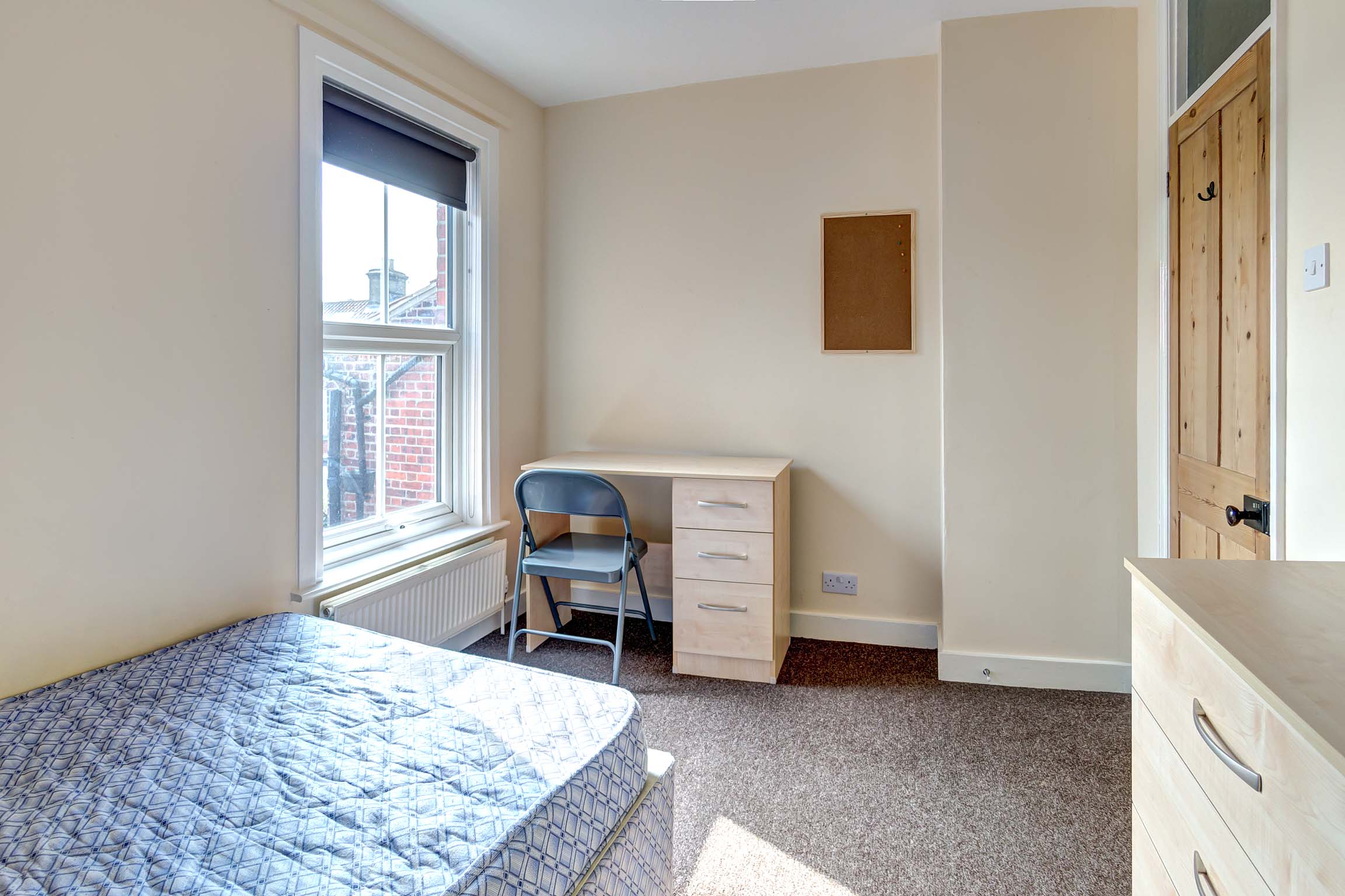 Double bedroom with wooden desk and chest of drawers and a divan bed.