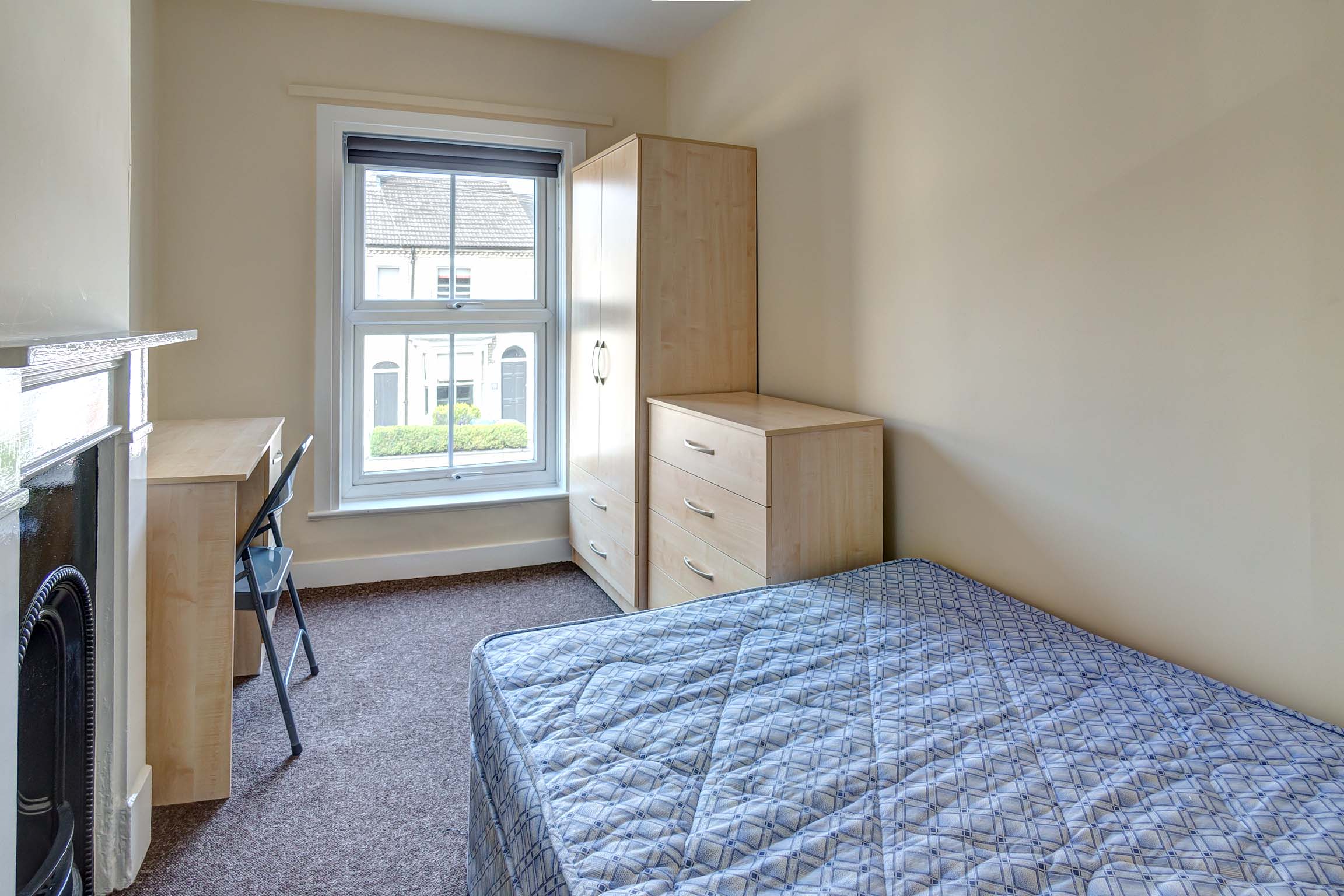 Double bedroom with divan bed, a decorative fireplace, a wooden wardrobe, desk and chest of drawers.