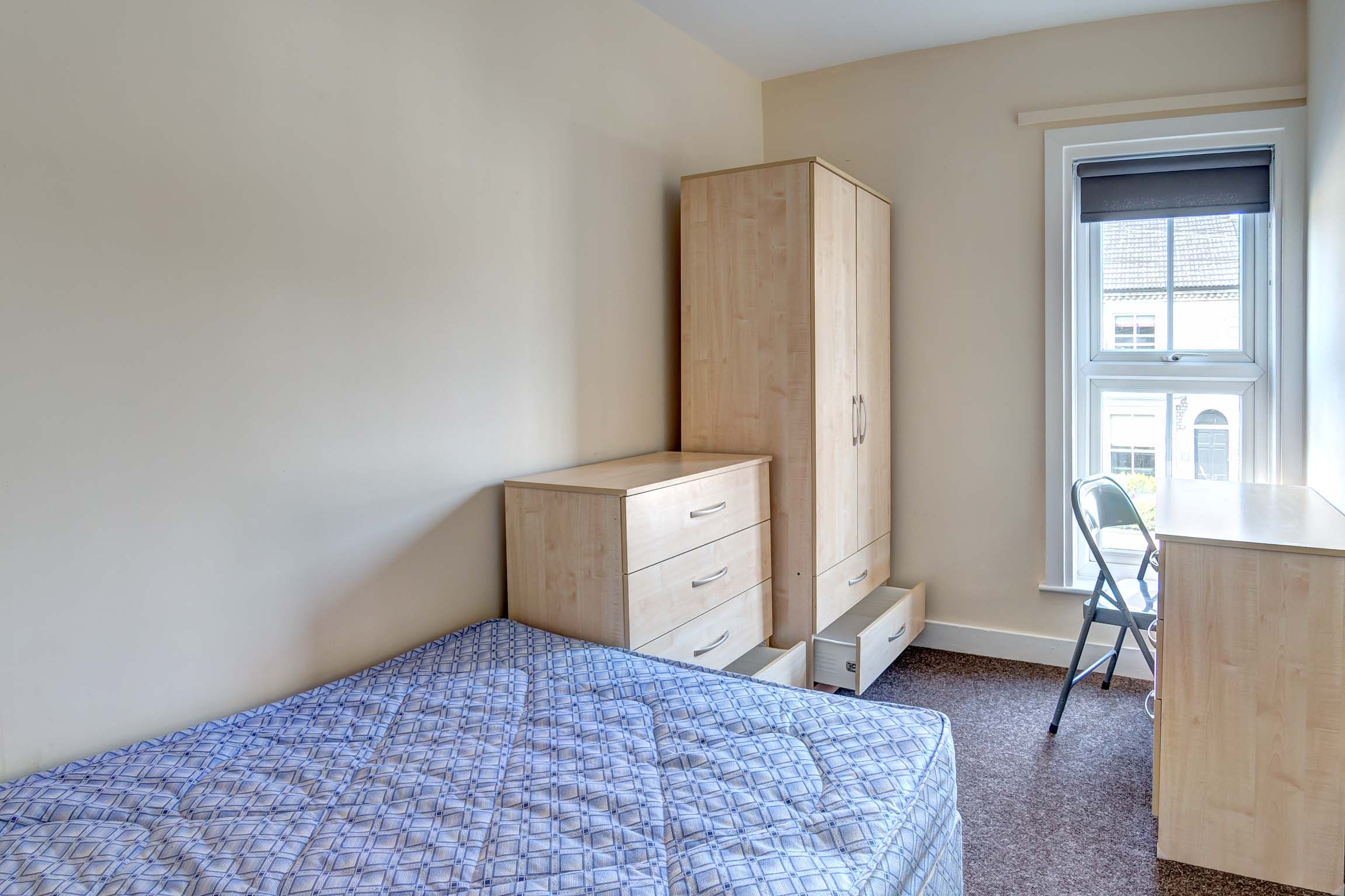 Double bedroom with divan bed, a decorative fireplace, a wooden wardrobe, desk and chest of drawers.