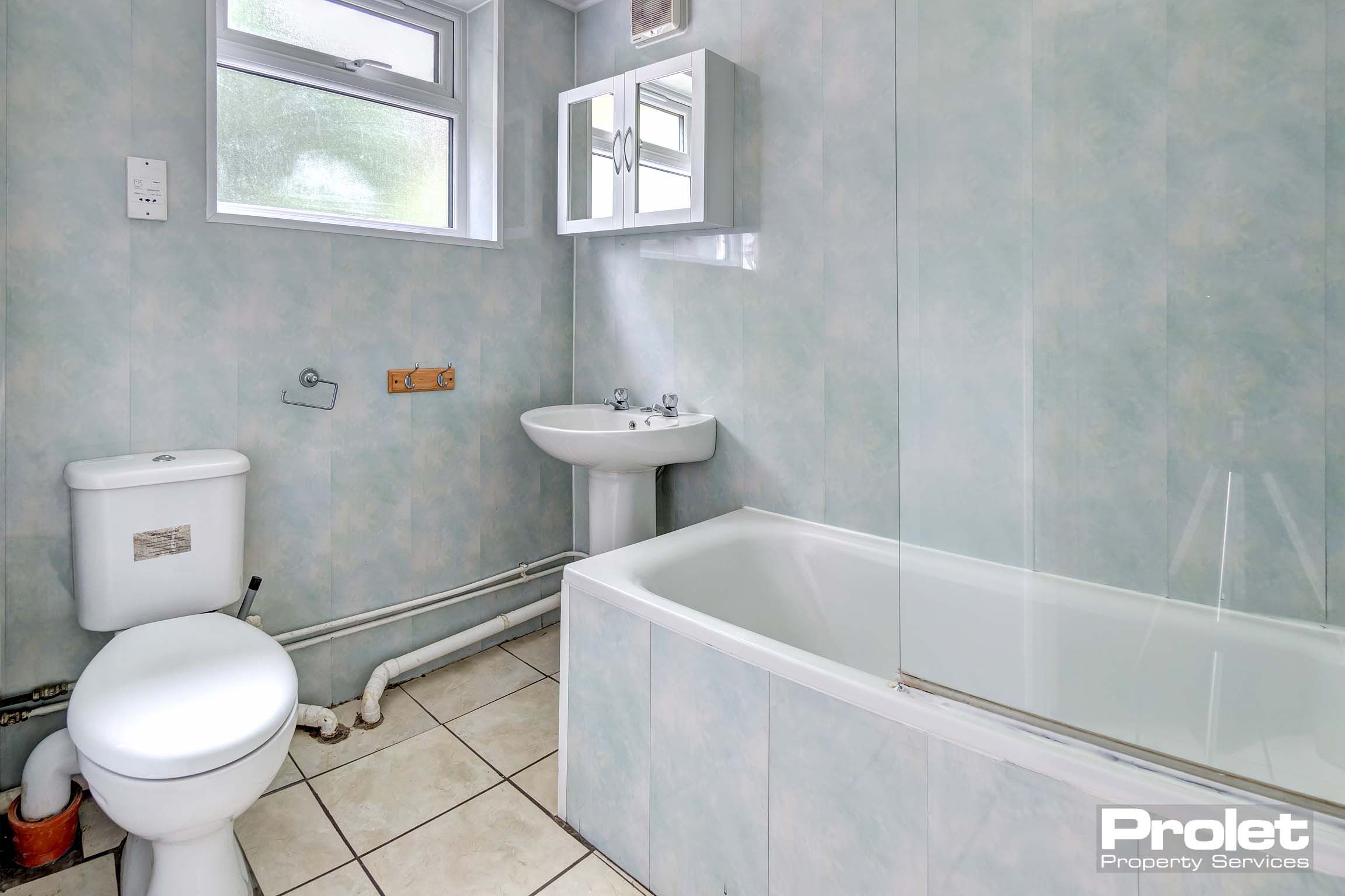 Grey coloured bathroom with a tiled floor. A white bath tub, sink and toilet - with a mirror above the sink. Shower above the bath.