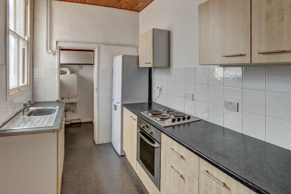 Galley kitchen with light coloured cabinets and black worktop