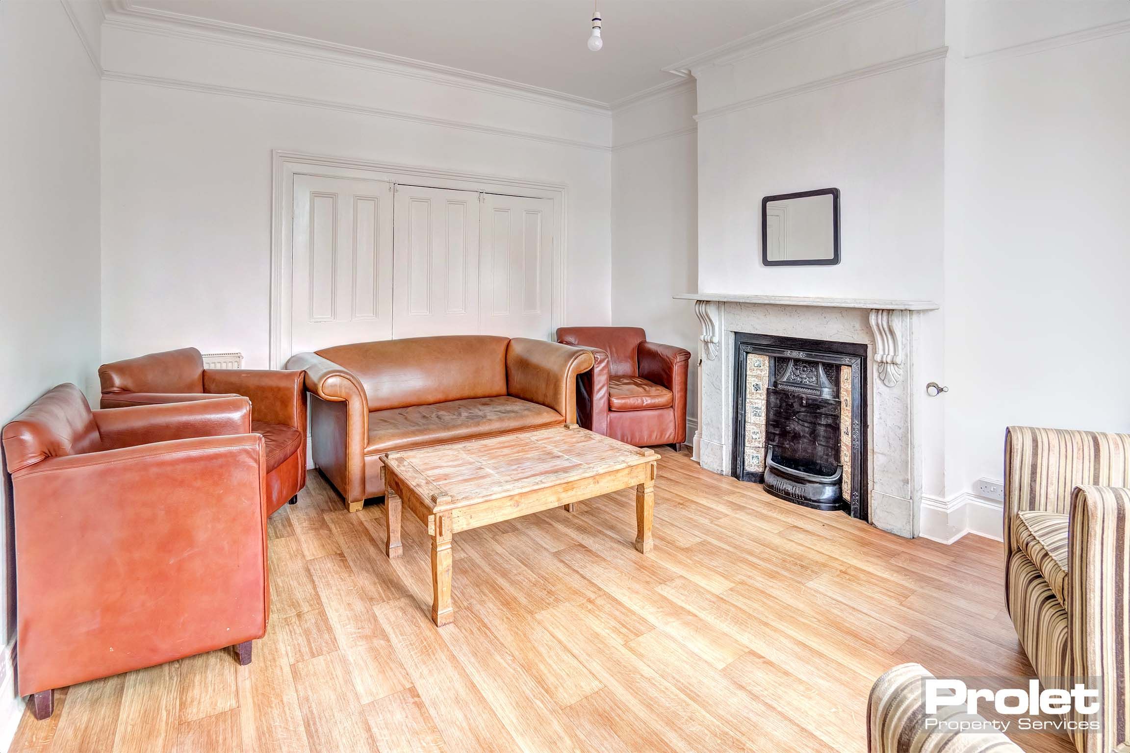 White lounge area with brown leather sofas and fabric sofas/chairs with decorative fireplace and a wooden coffee table.