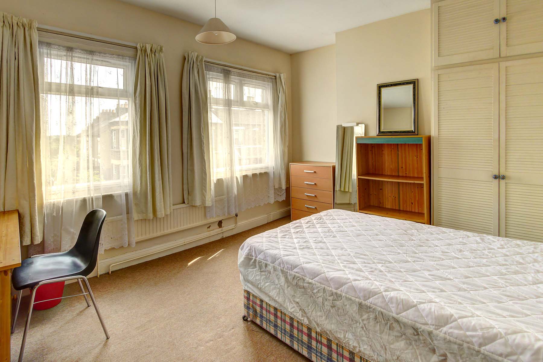 Large bedroom with a double divan bed base and mattress, a wooden bookcase and chest of drawers and a wooden desk and black chair.