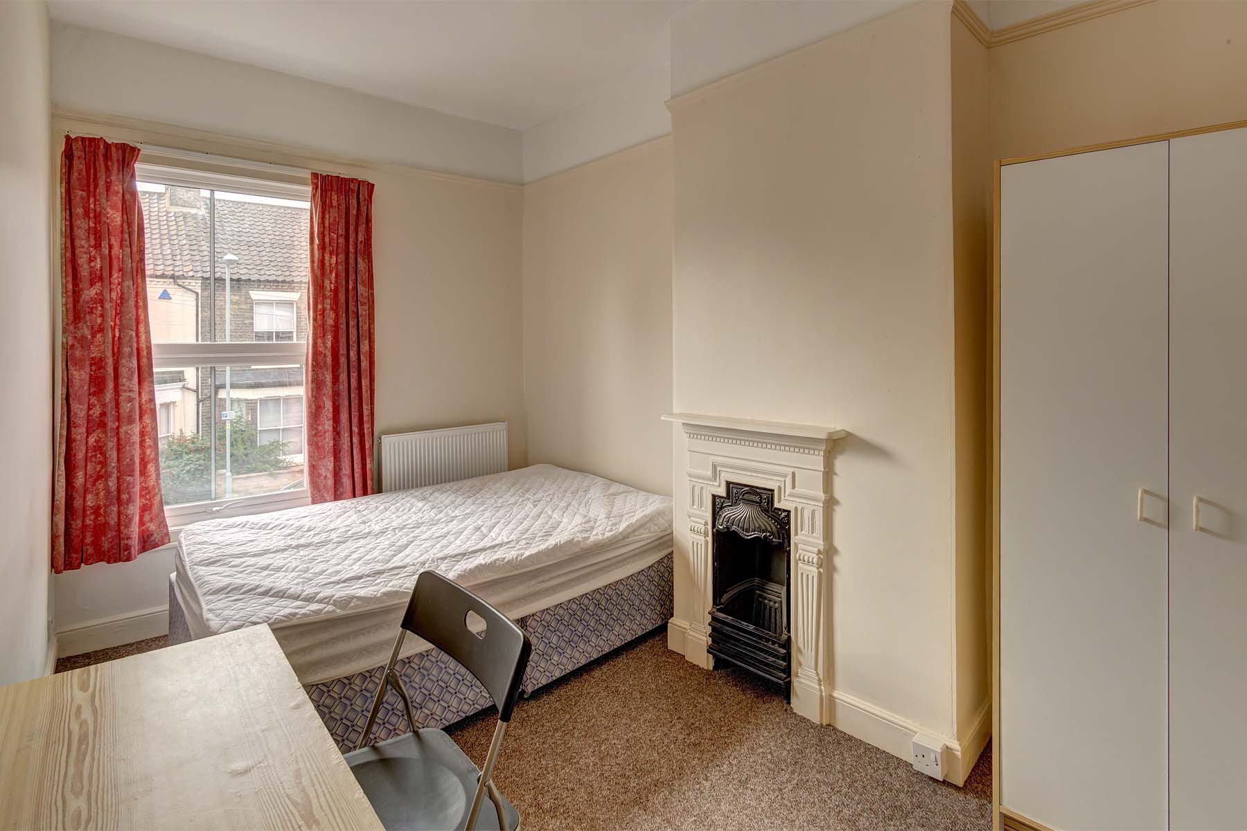 Magnolia painted bedroom with decorative fireplace, white wardrobe, wooden effect desk with a black chair and a divan bed.