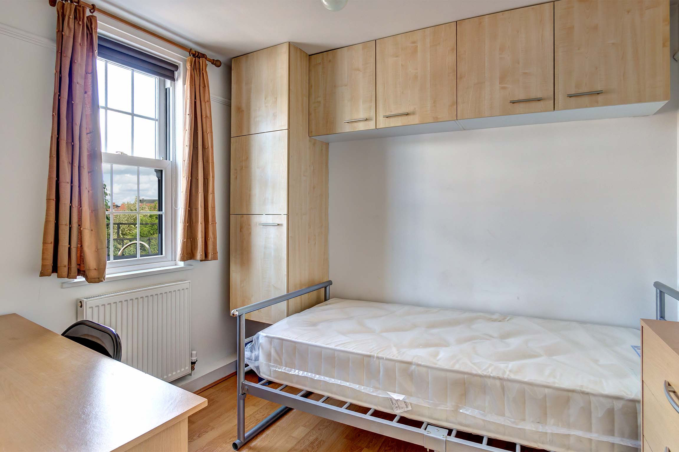 Bedroom with metal bed frame, fitted wooden storage units, wooden desk.