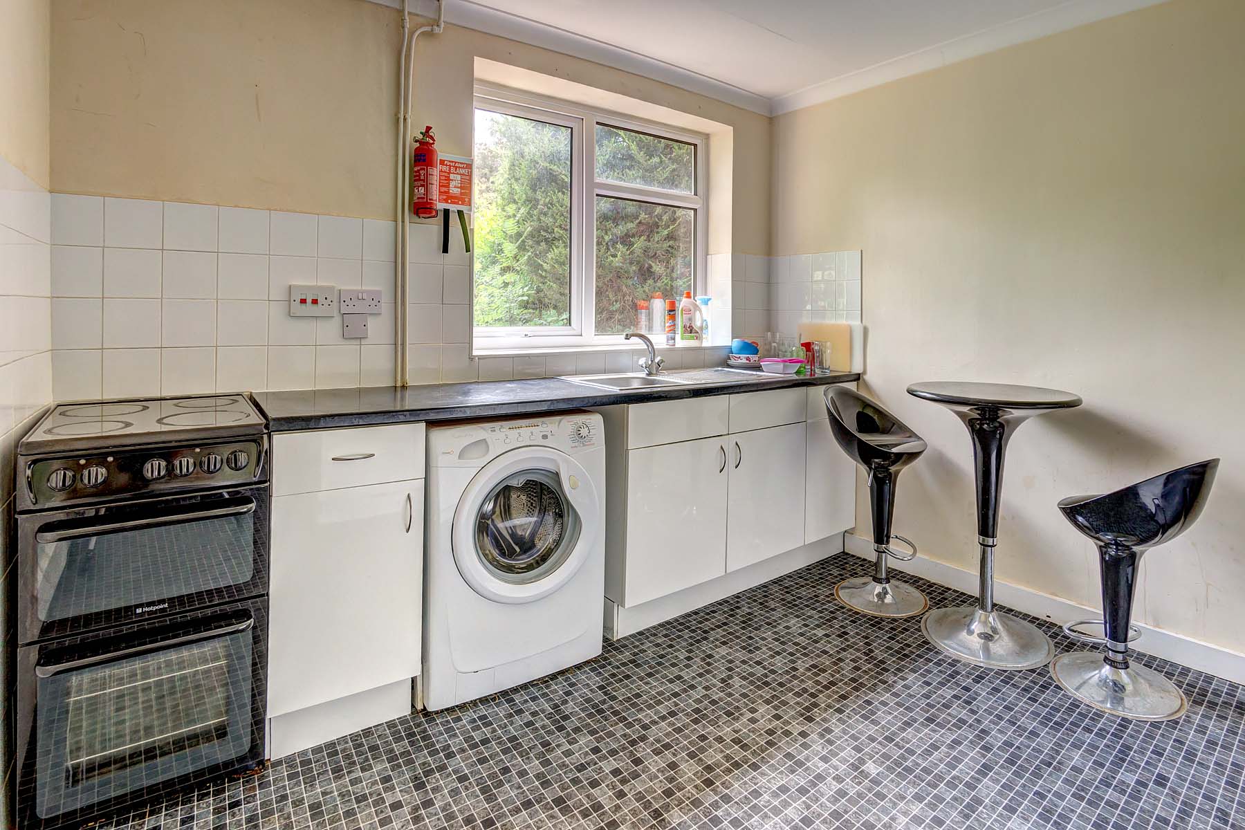 White fitted kitchen with an oven and a washing machine. A breakfast table with two chairs.