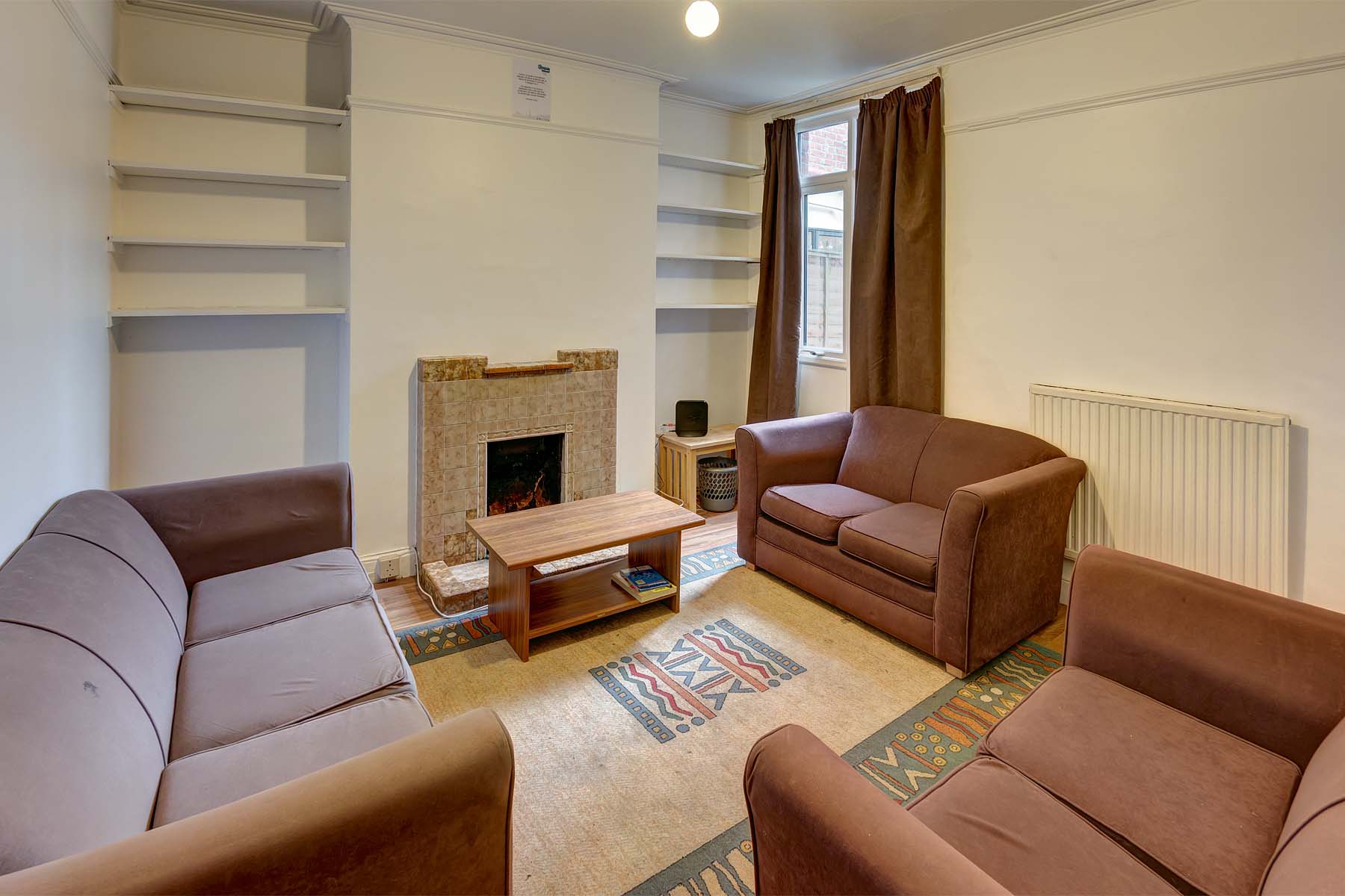 Lounge area with decorative fireplace and built in shelving. Three brown fabric sofas.