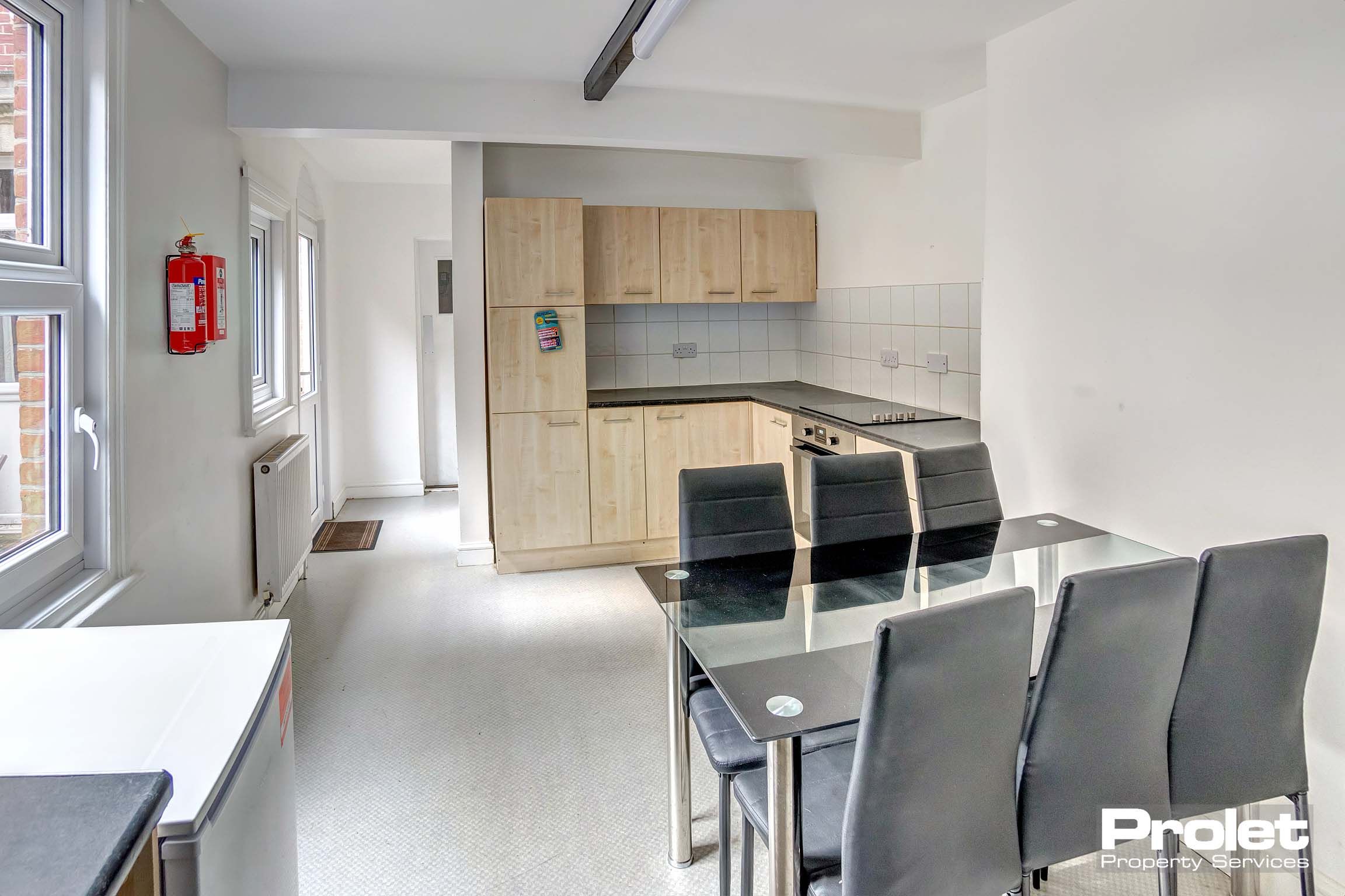 White painted kitchen and dining area. Wooden fitted kitchen with a black glass table and set of chairs.