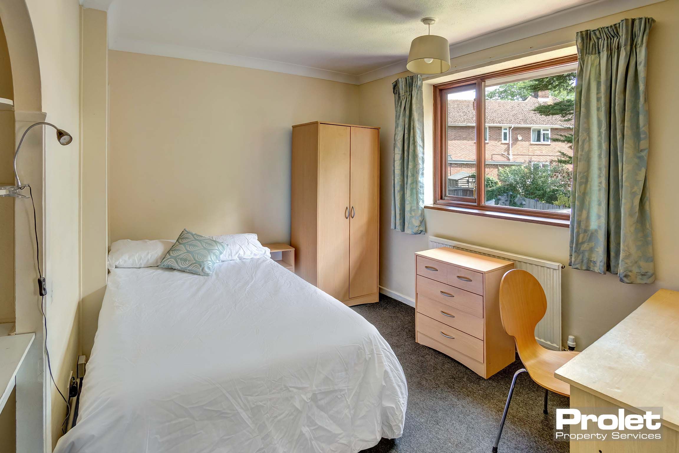 Double bedroom with wooden wardrobe, desk and chest of drawers.