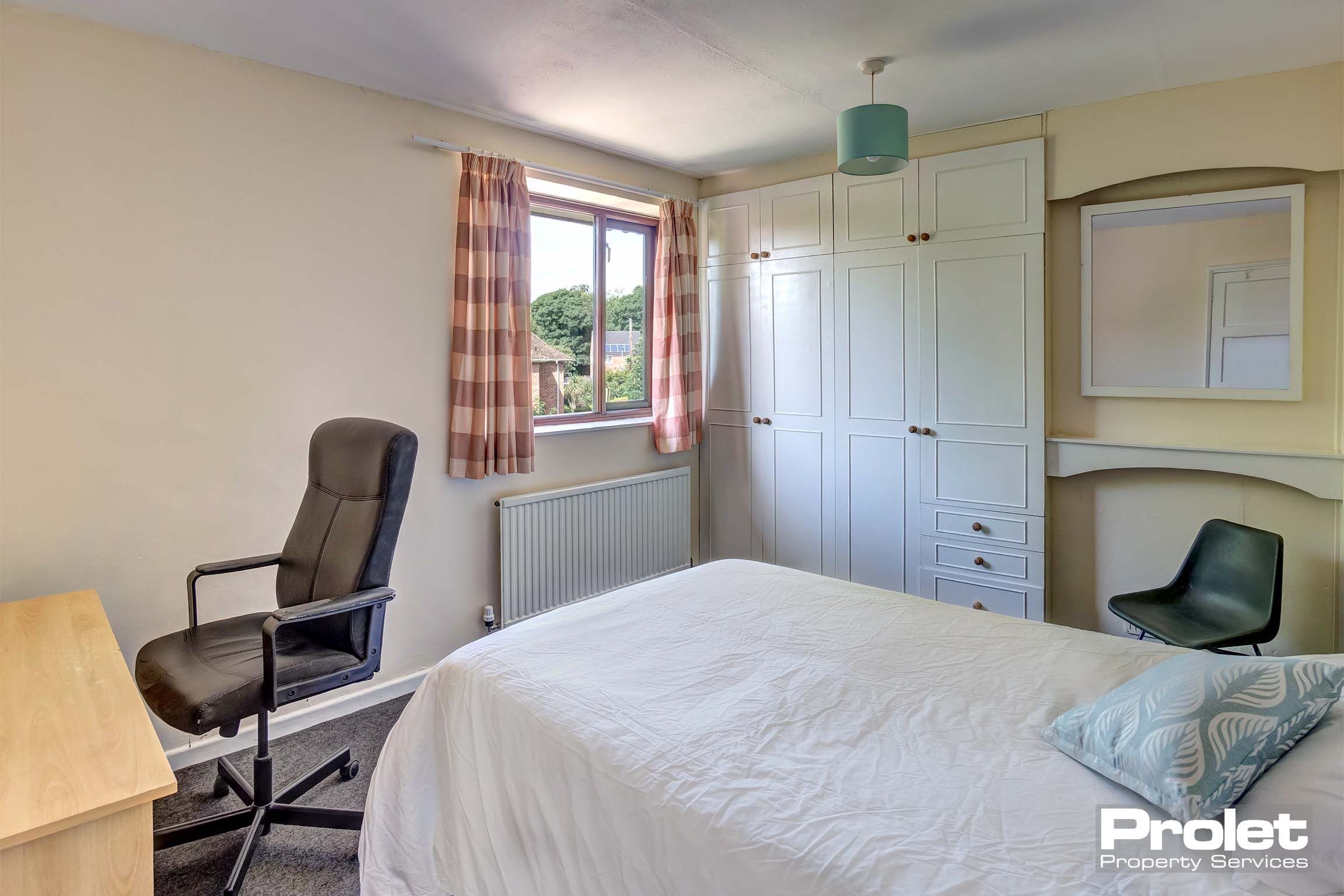 Double bedroom with built in wardrobes, a wooden desk and a double bed and mattress.