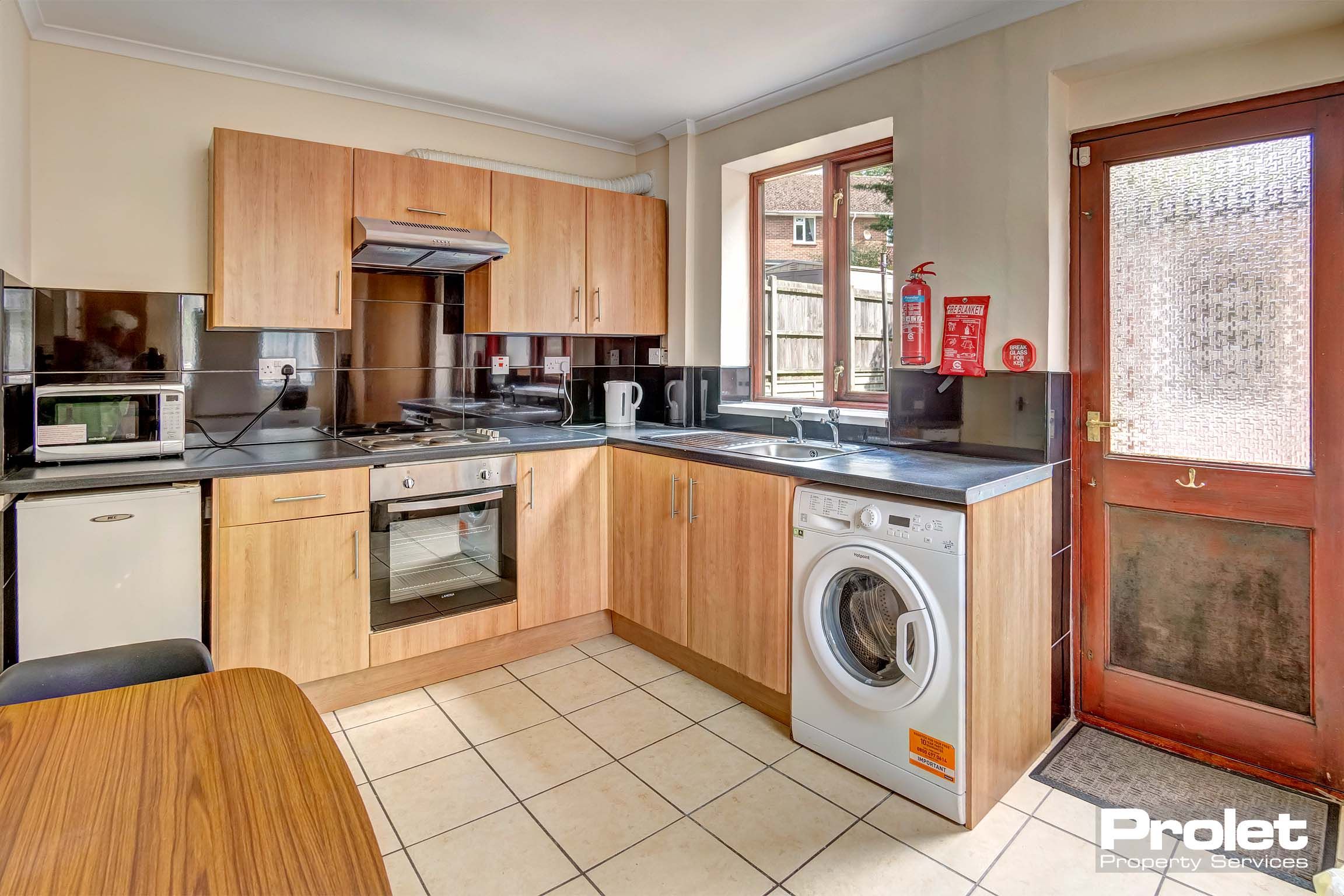 Wooden fitted kitchen with black grain worktop and tiled flooring.