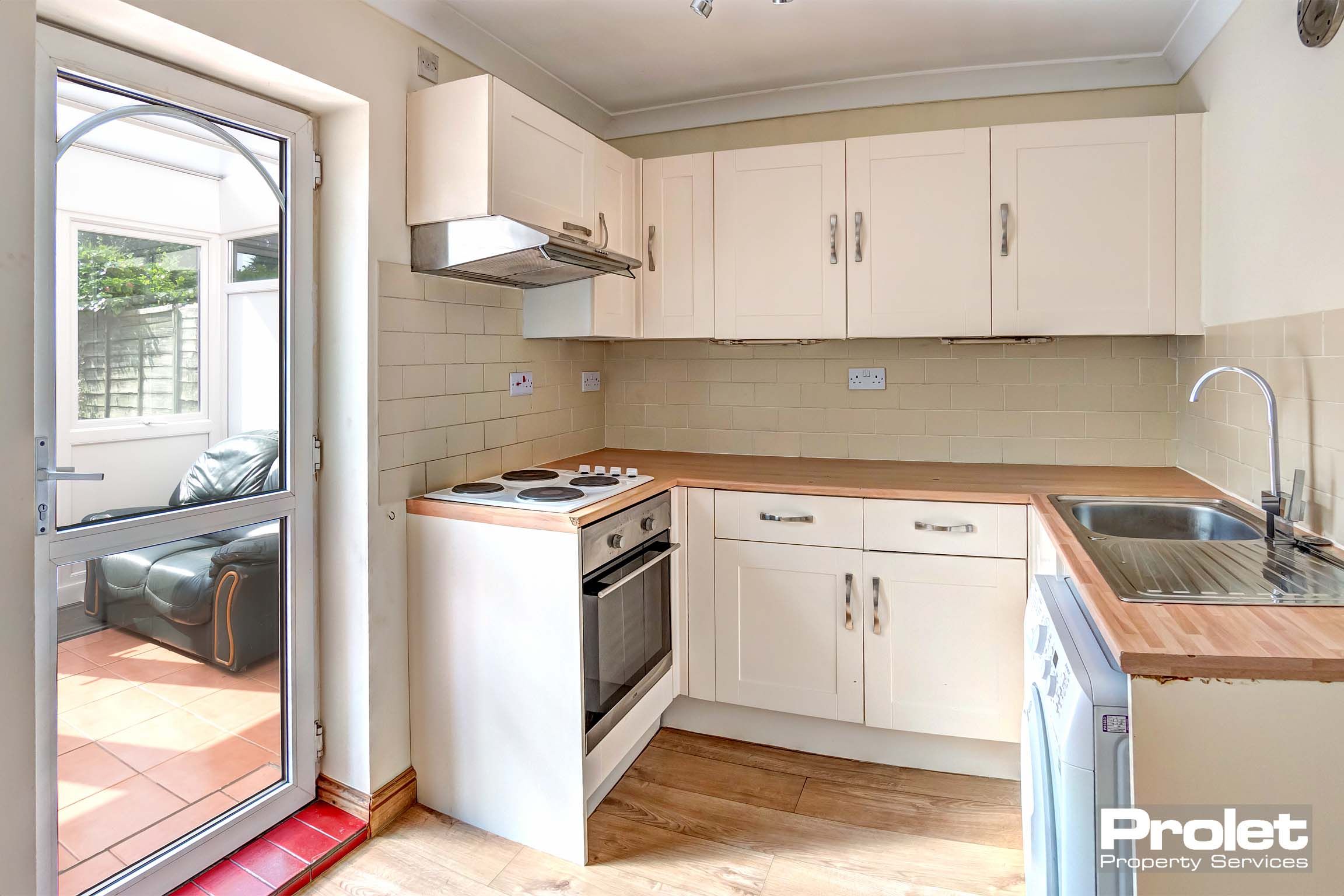 Kitchen with white cabinets and wood effect worktops, leading to conservatory