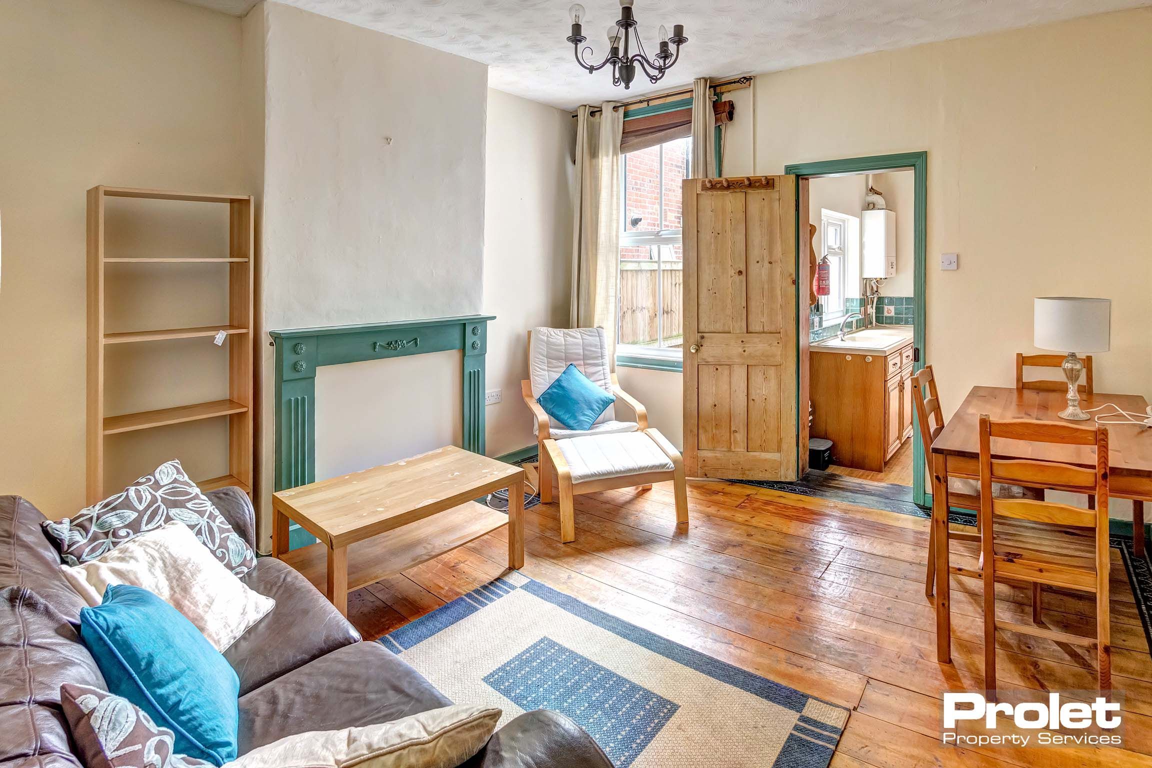 Living room, leading to kitchen, with wooden floors, sofa and armchair.