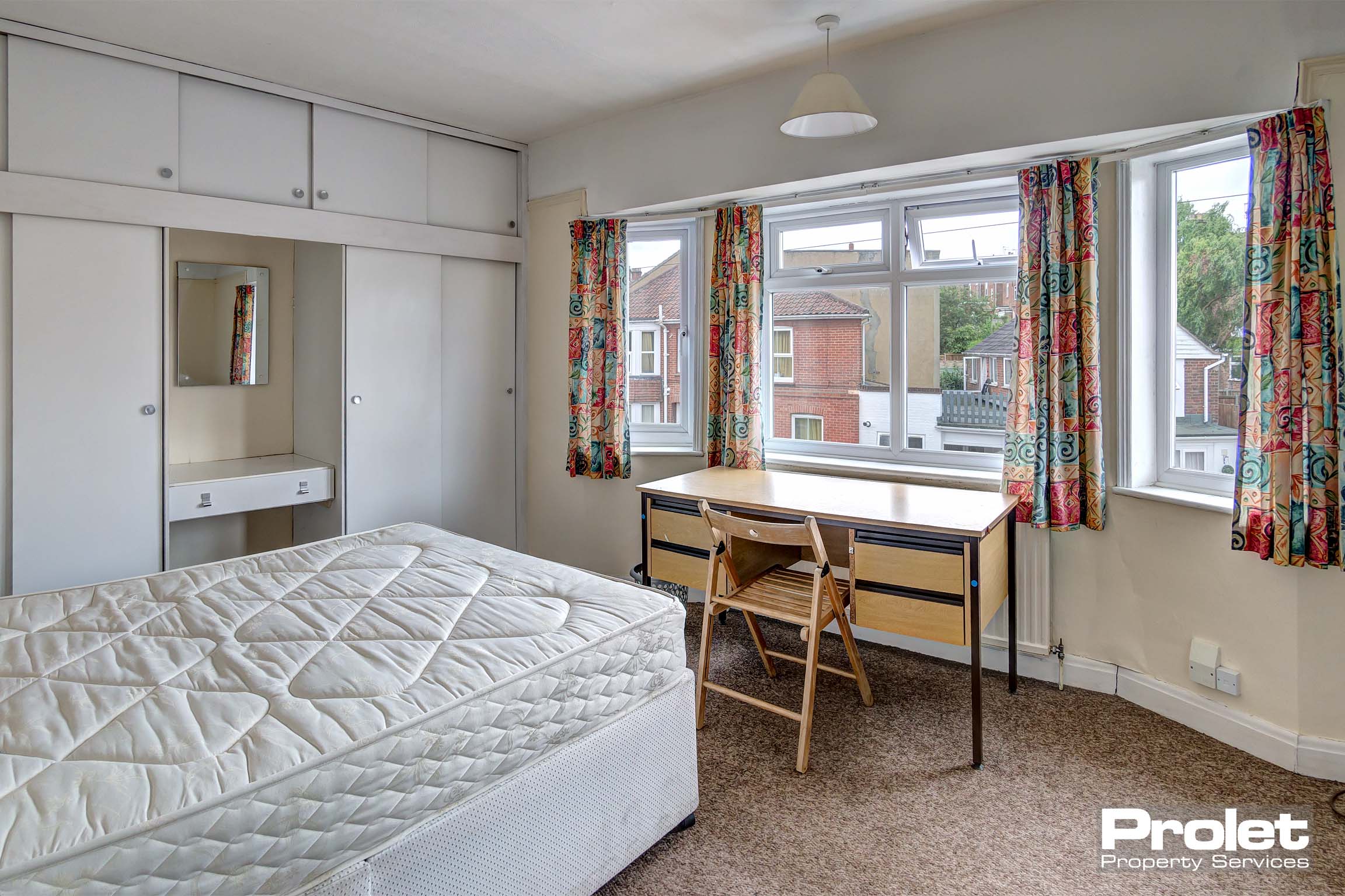 Large double bedroom with built in white wardrobes/storage space. A wooden desk and chair and a divan bed with mattress.