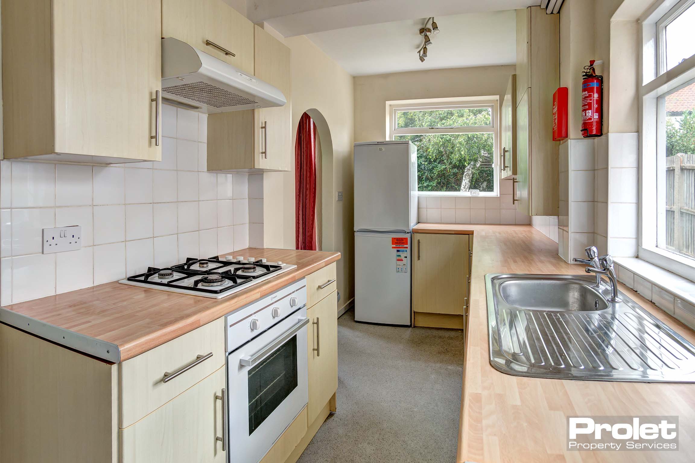 Galley style kitchen with built in wooden units and a fridge/freezer, an oven with extractor fan and a silver sink.