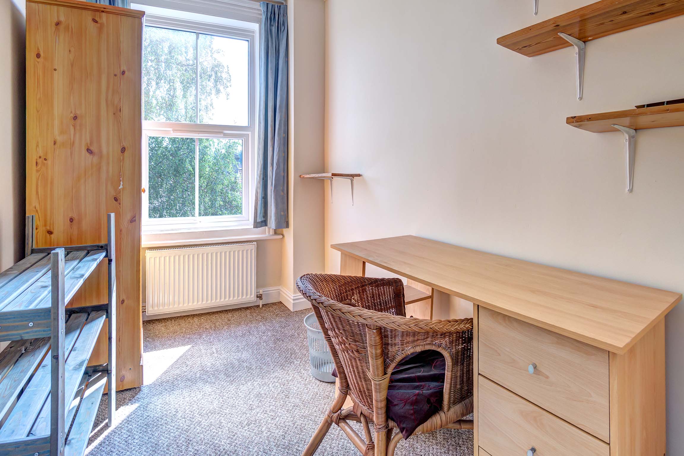 Study room with wooden desk and chair, a wooden storage unit and shelves on the wall.