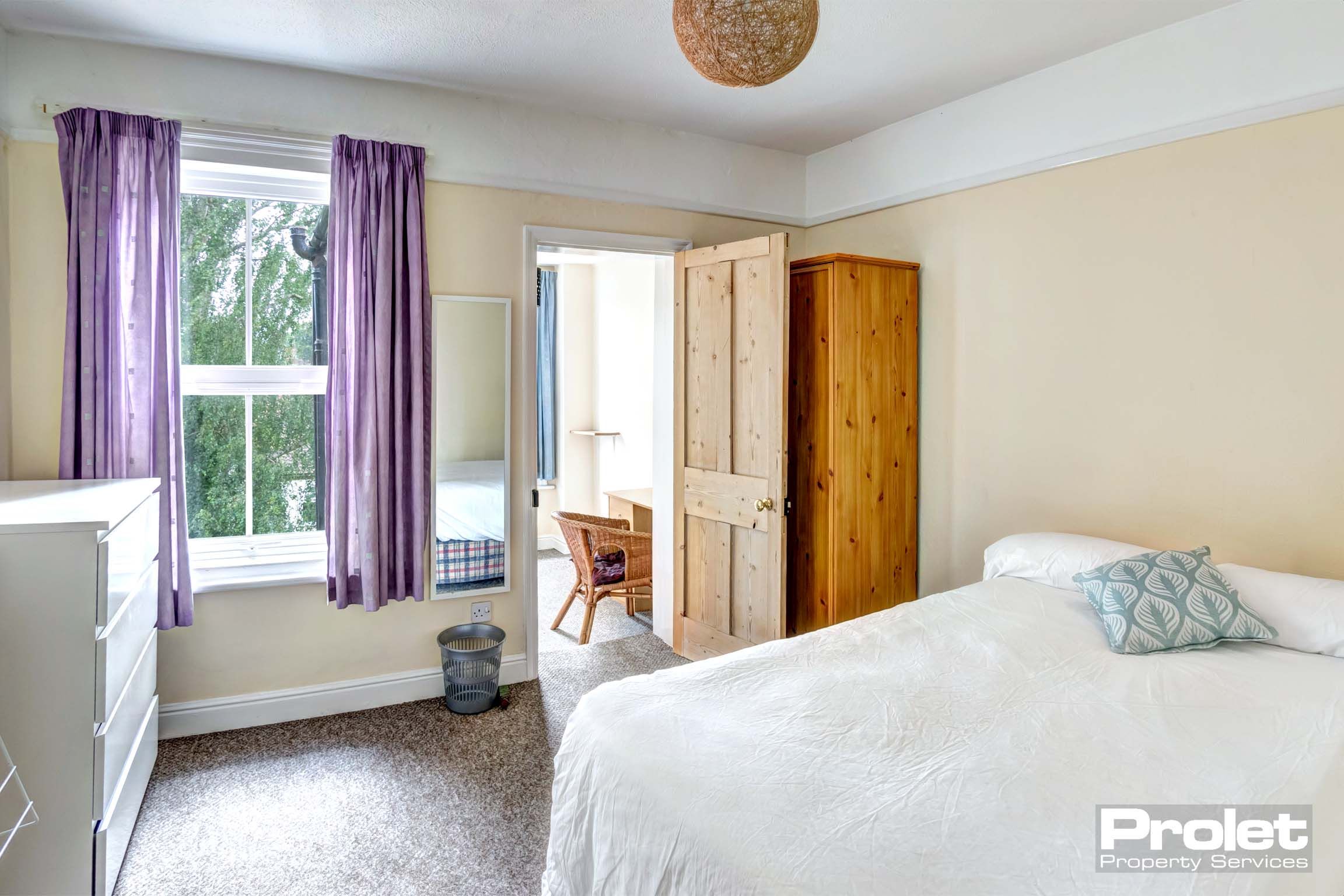 Double bedroom with white chest of drawers, a wooden wardrobe and a wooden door for entry to the study room.