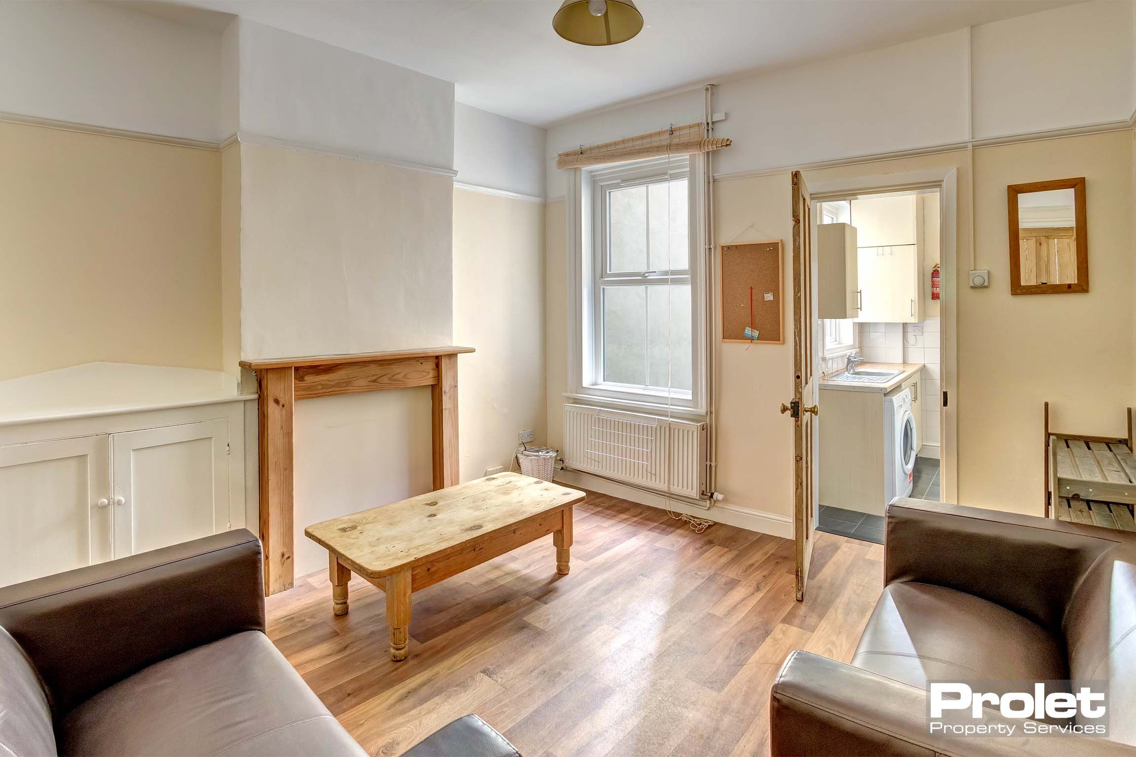 Lounge area with wooden flooring, two brown leather sofas, a wooden coffee table and white panelling walls.