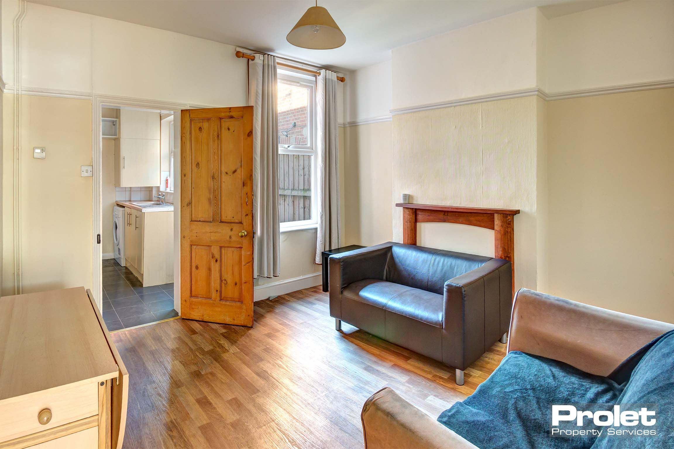 Living room with sofas and hardwood floor, leading to kitchen