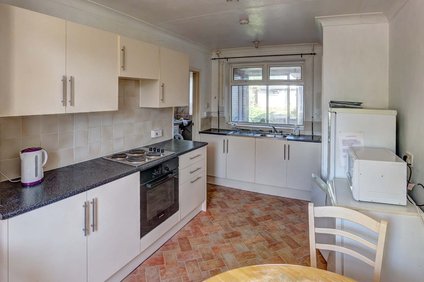 Kitchen with white cupboards, black worktops, a dining table, and white goods