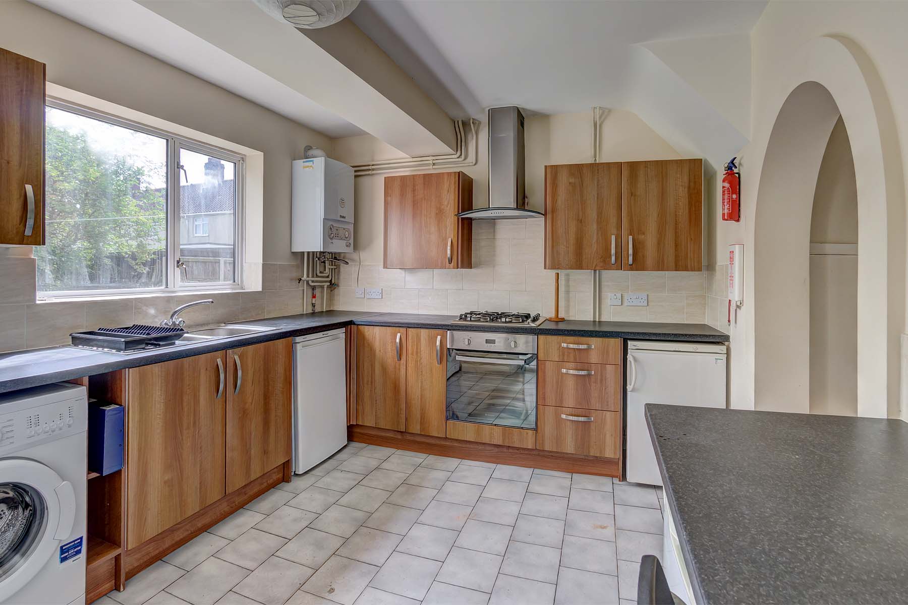 Kitchen with white tiled floor, wooden cabinets, white goods, and breakfast bar