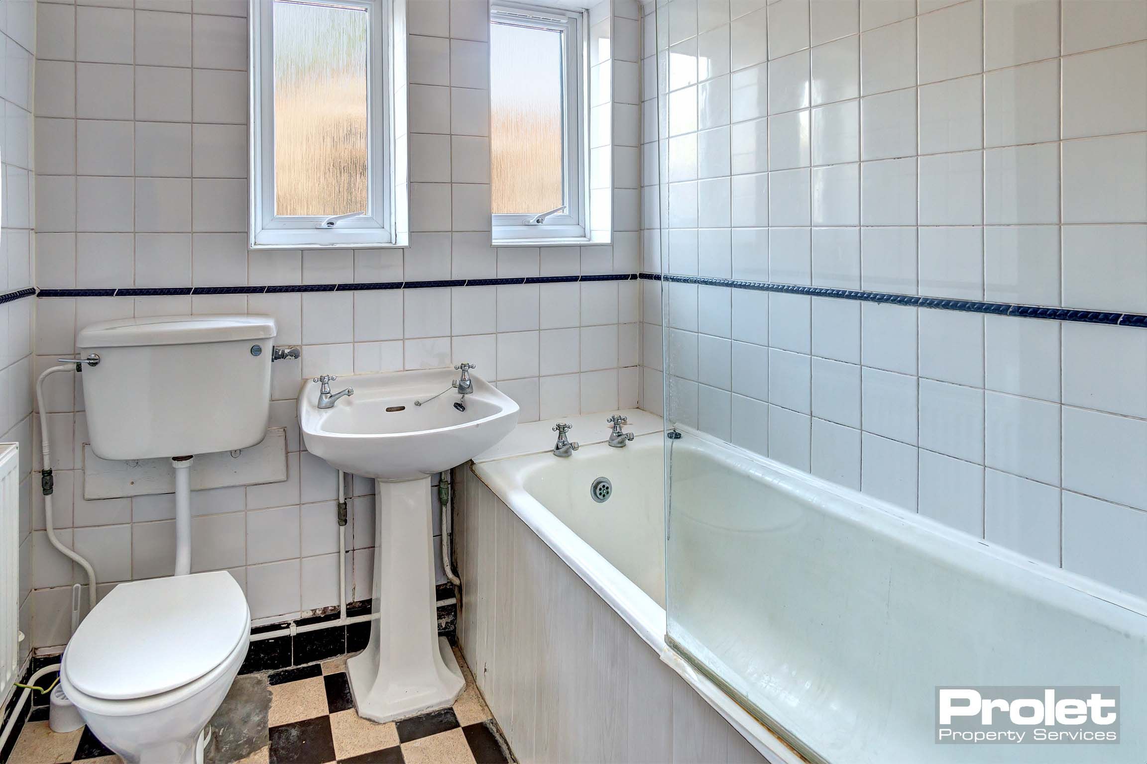 Bathroom with black and white tiled floor, shower over bath, sink, and toilet