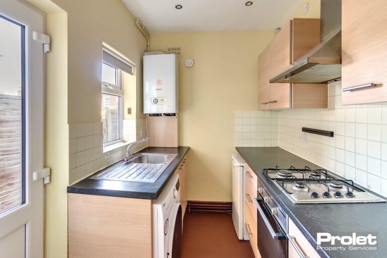 Buttermilk walls with beech effect units and black work top with oven, fridge freezer and washing machine