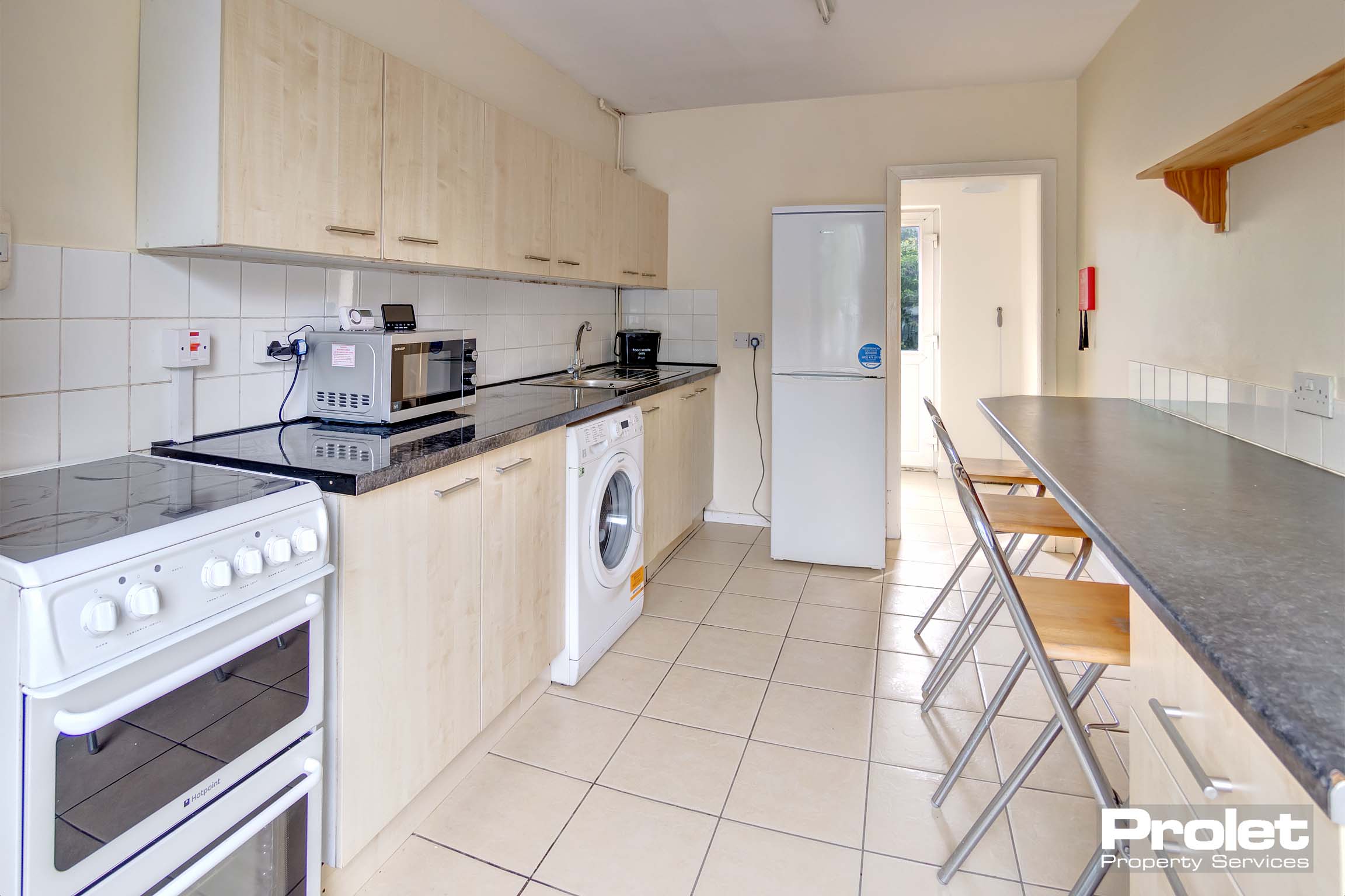 Kitchen with breakfast bar, black worktop, and light wood cupboard.