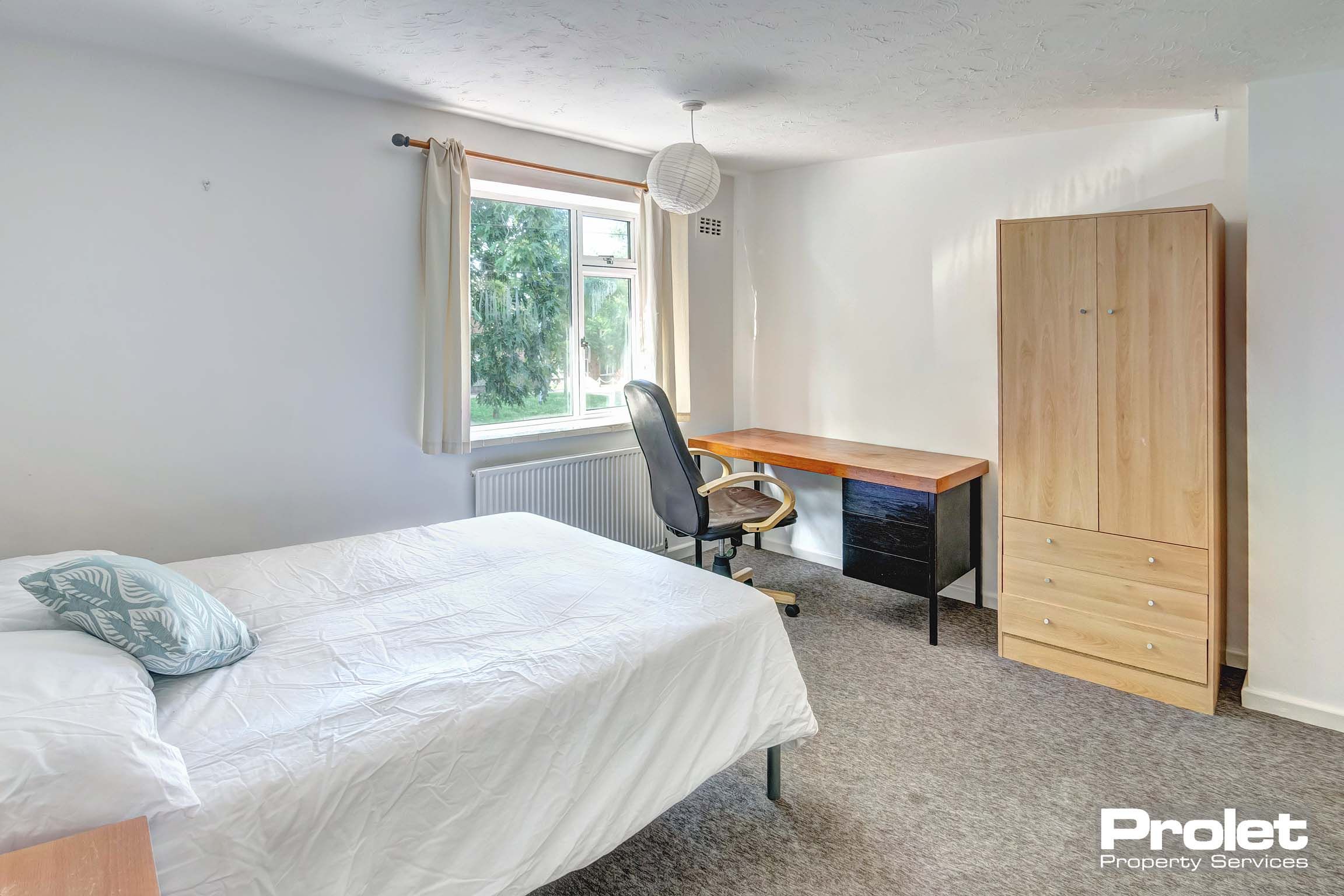 Large double bedroom with metal bed frame, a wooden wardrobe and desk with an office style chair.