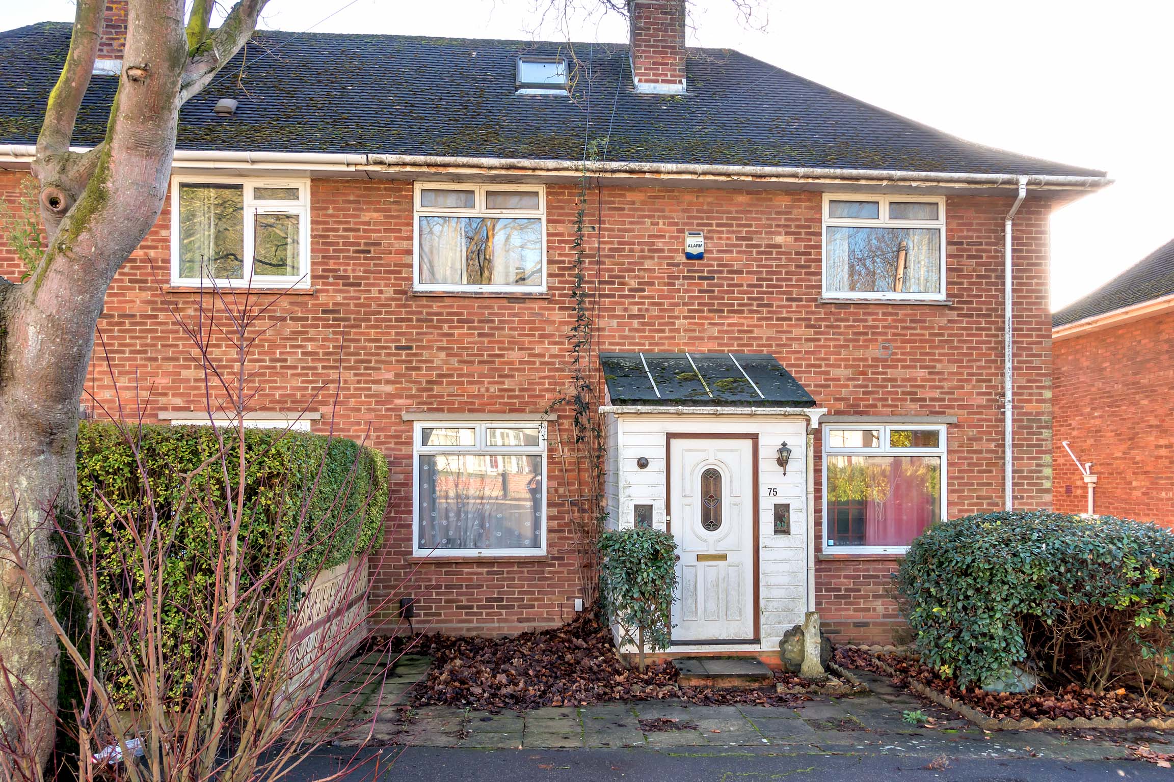 Red brick, terraced house with a driveway and a white porch with white door.