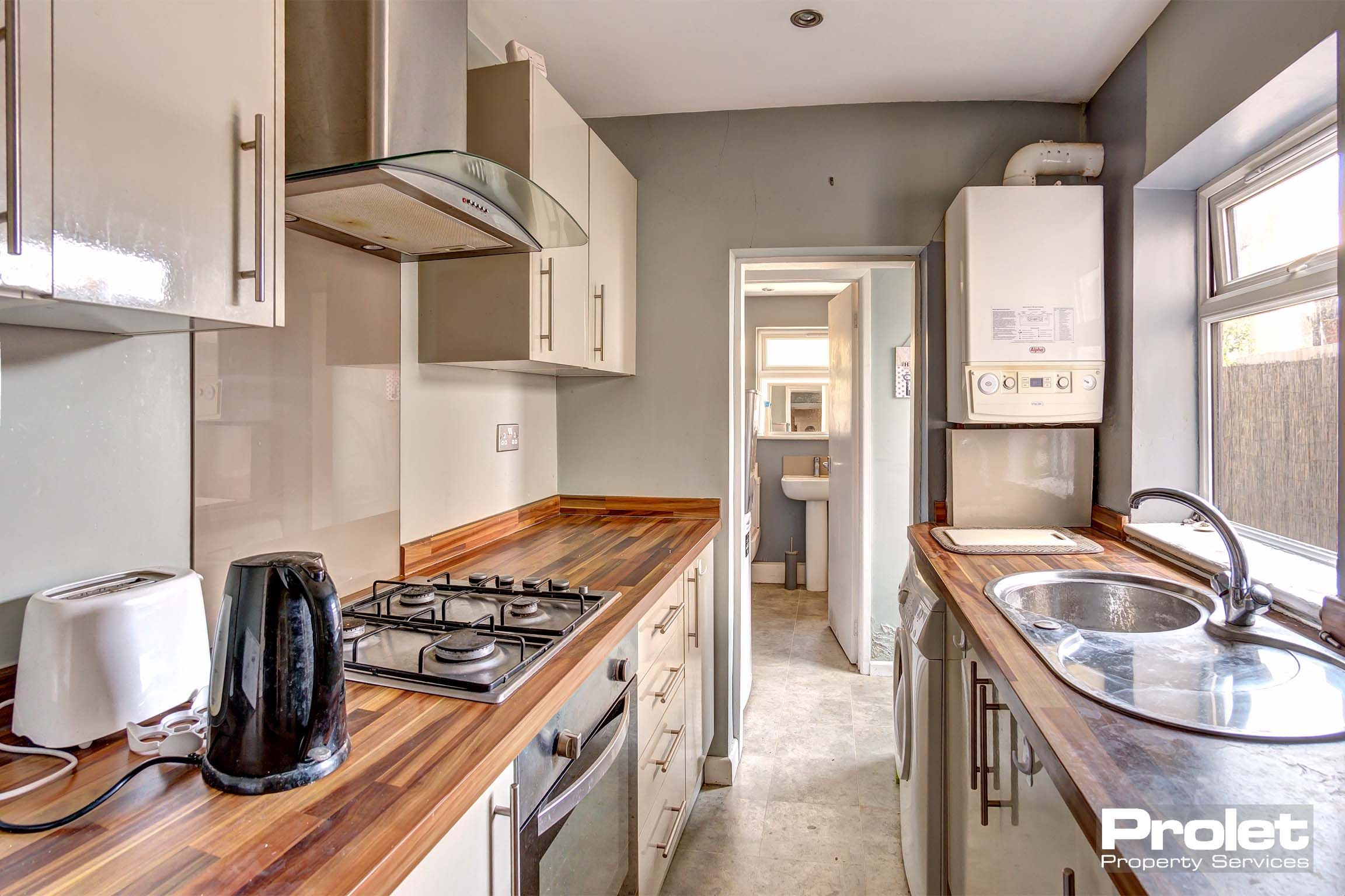 Galley style kitchen with cream coloured fitted kitchen and wooden look worktop.