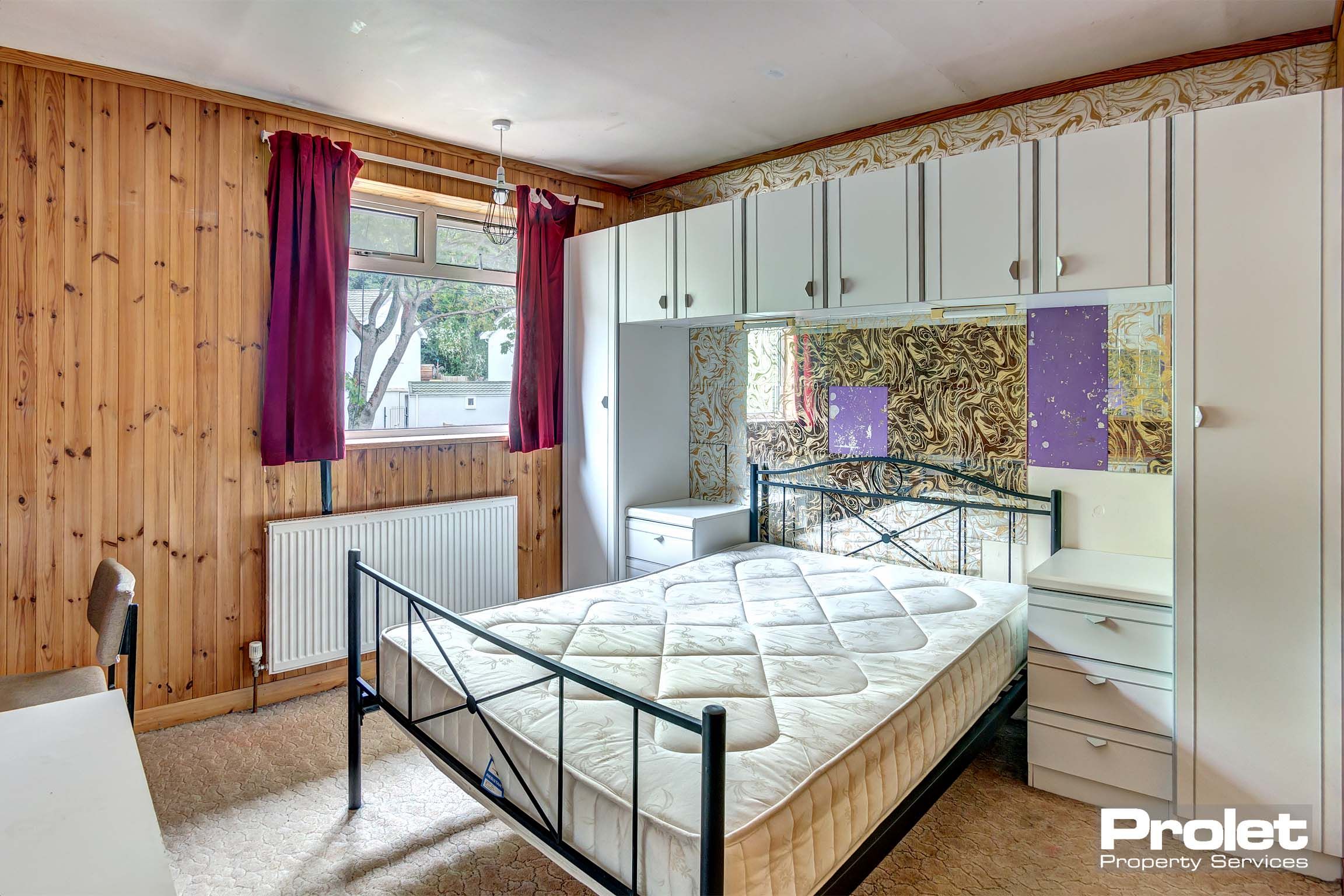 Large double bedroom with built in storage cupboards, wooden panelled walls and a metal double bed frame.