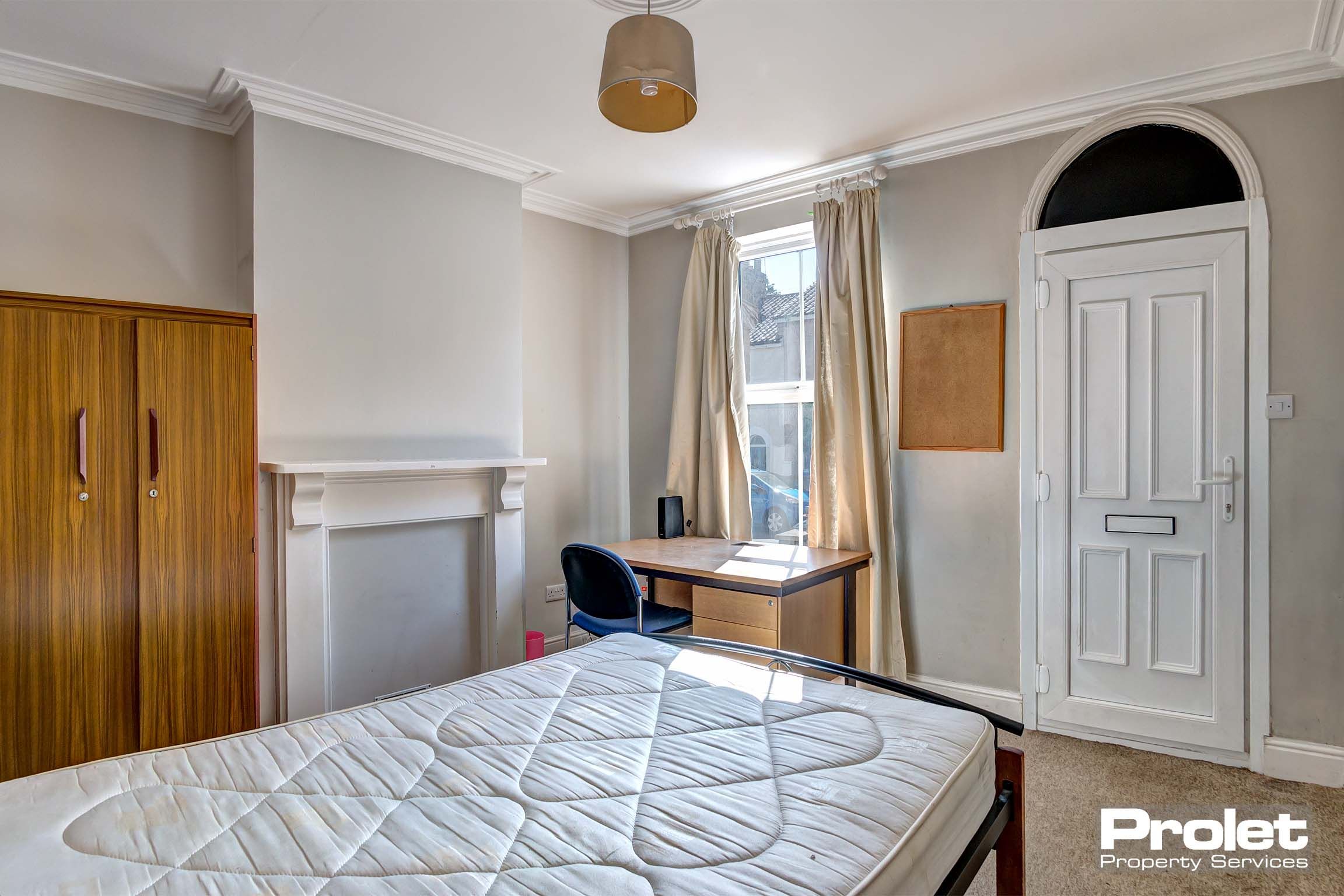 Front bedroom with double bed, wooden wardrobe, wooden desk and mantlepiece.