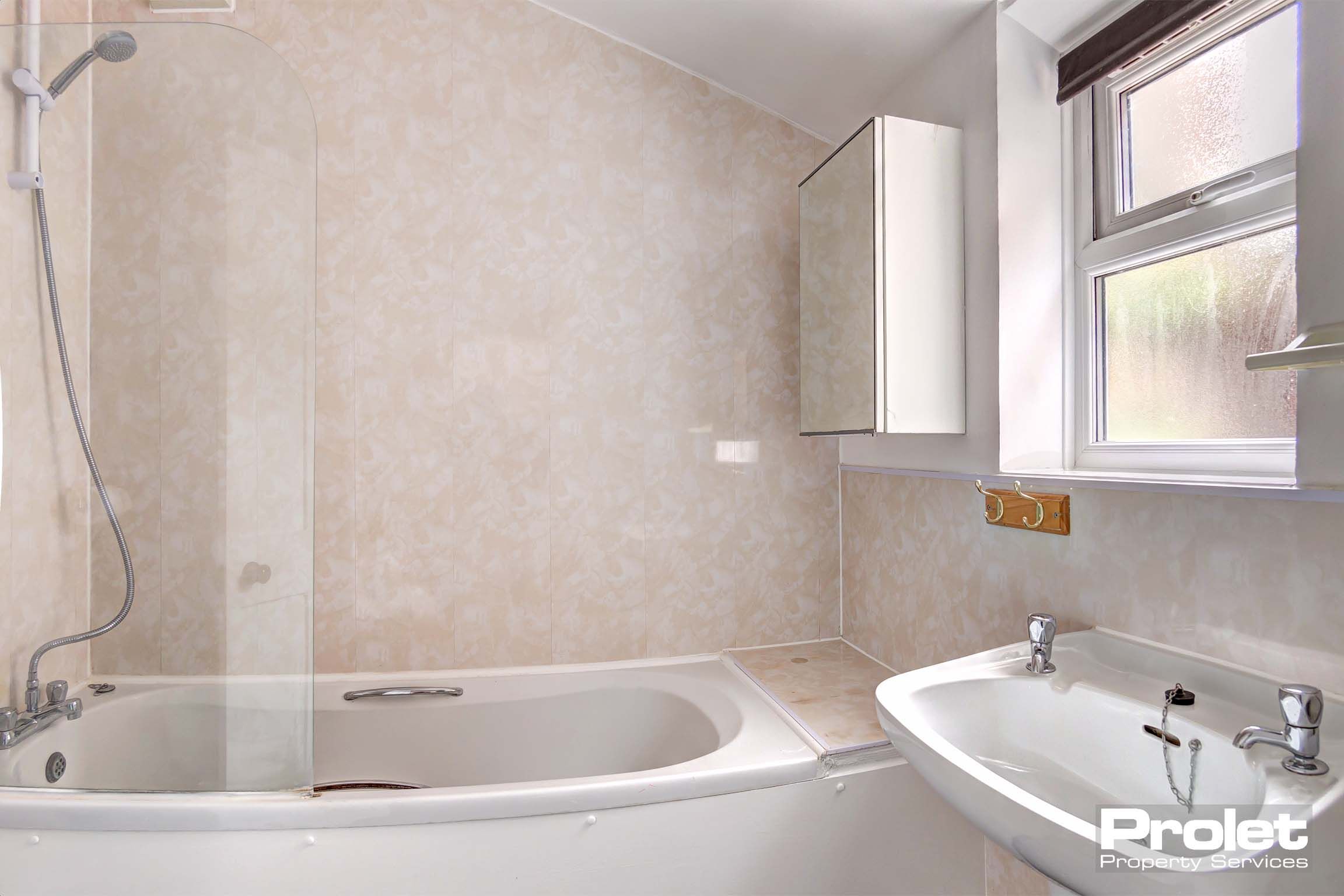 Bathroom with white sink and bath tub with shower over the bath.