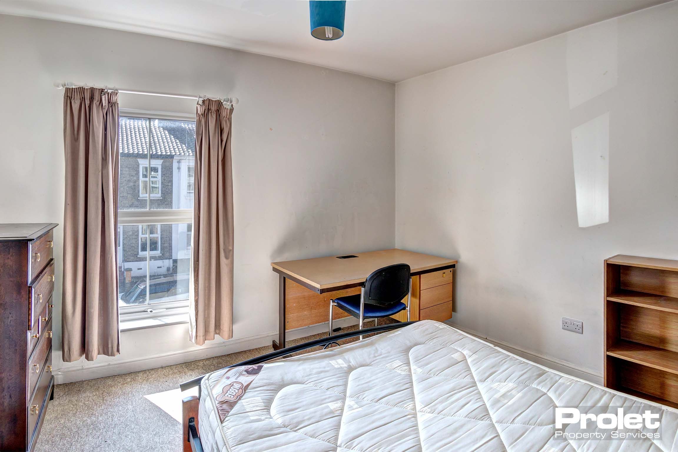 Bedroom with double bed, wooden chest of drawers, a wooden bookshelf and a wooden desk with office chair.