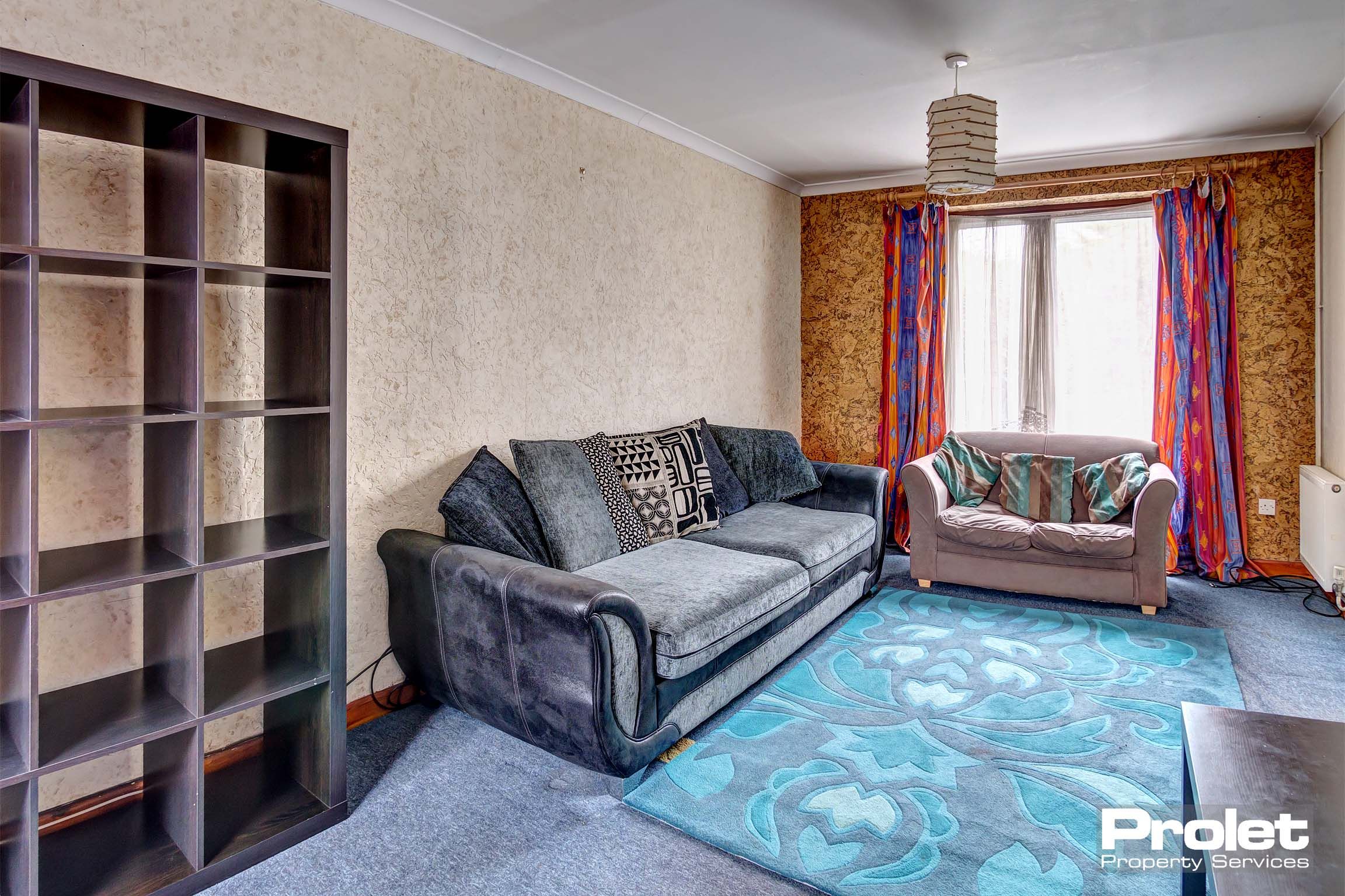 Lounge area with magnolia walls, a blue carpet and rug and one black leather sofas and one camel coloured fabric sofa. Cube storage unit.