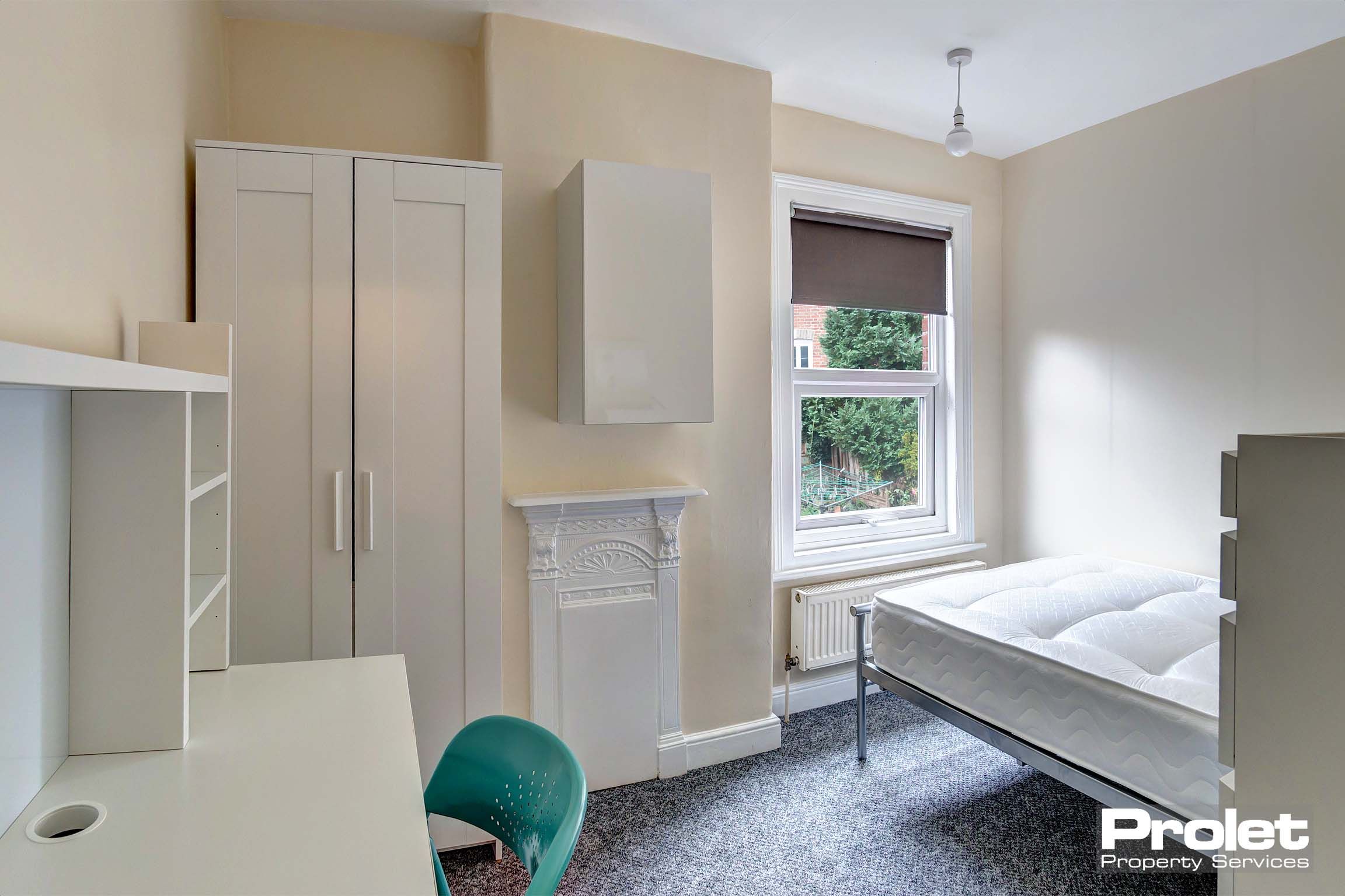 Double bedroom, magnolia painted walls. White wardrobe with matching desk and chest of drawers. White cupboard for storage fixed to the wall.