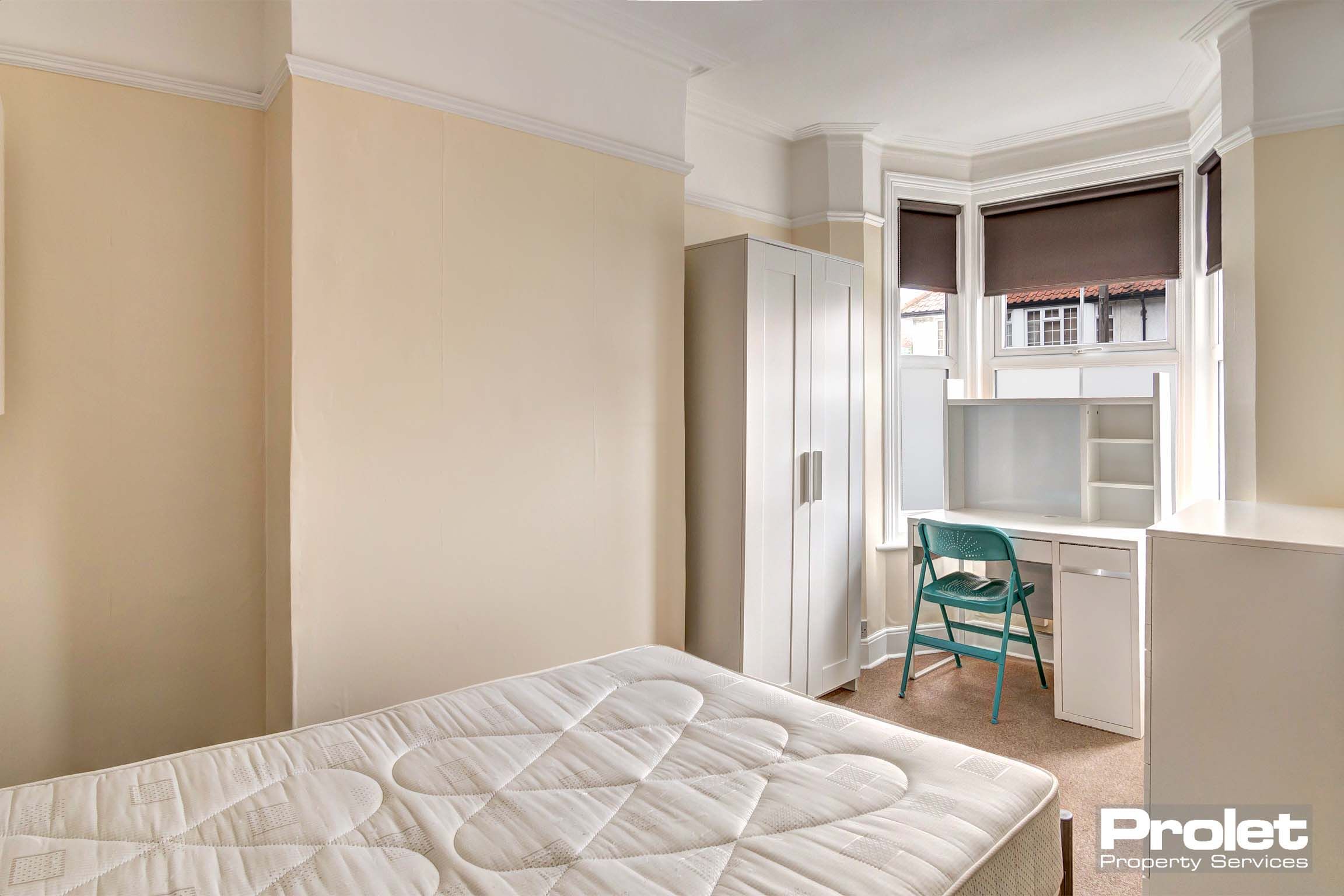 Double bedroom with magnolia painted walls. A white wardrobe with matching desk and chest of drawers.