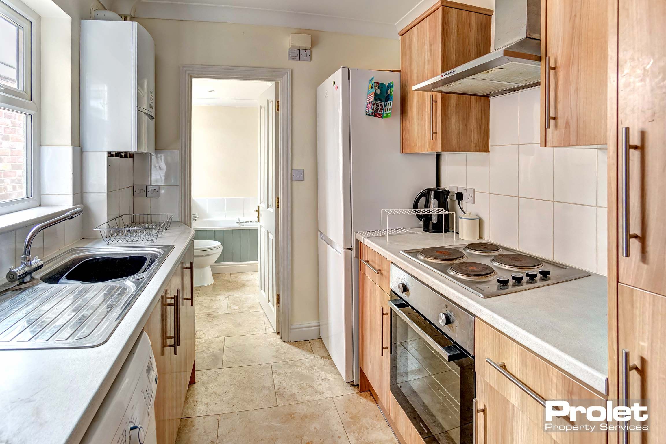 Galley kitchen with wood effect cabinets, leading to bathroom