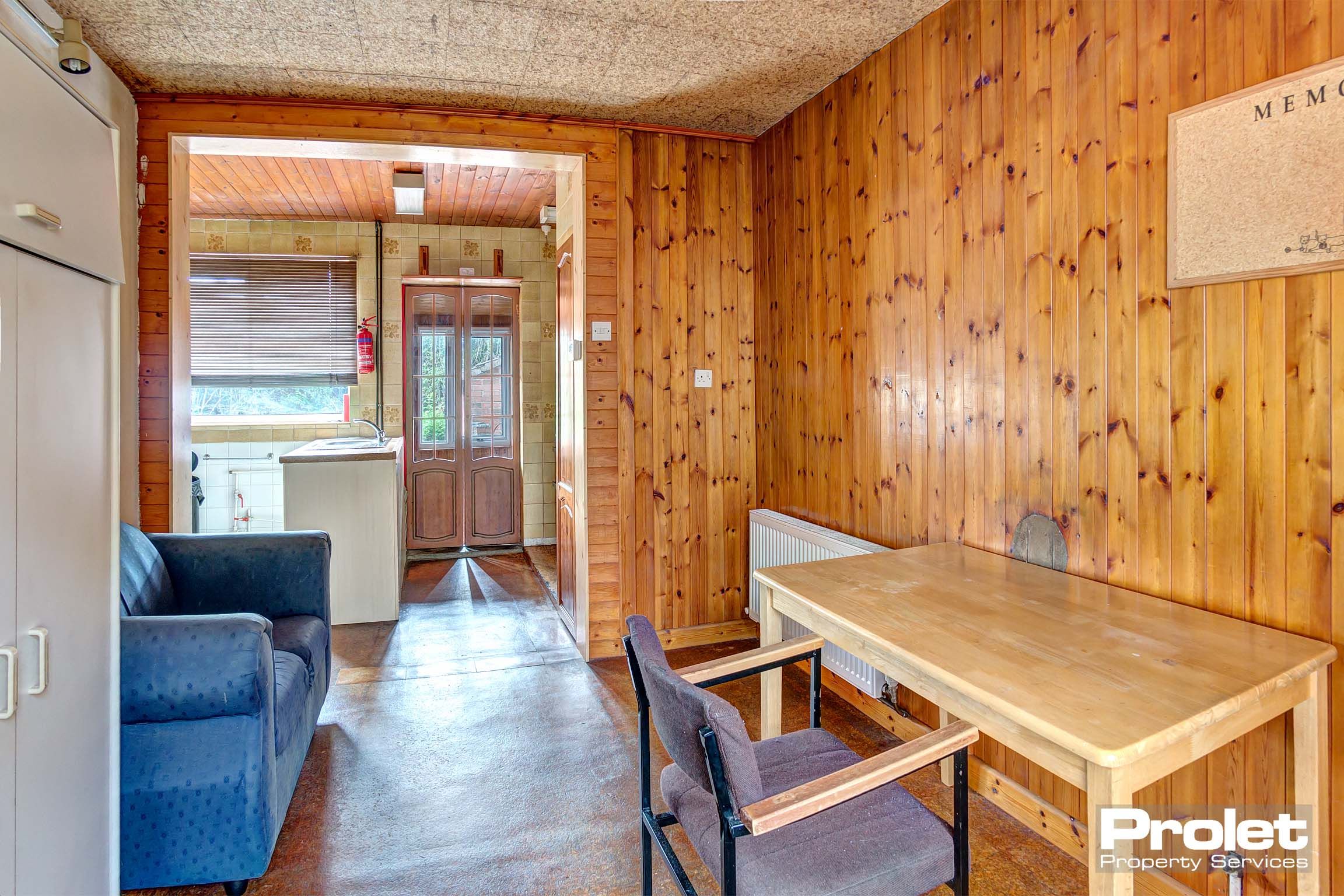 Dining area with wooden panelled walls, a tiled flooring and built in storage cupboards. A wooden dining table and a blue leather sofa.