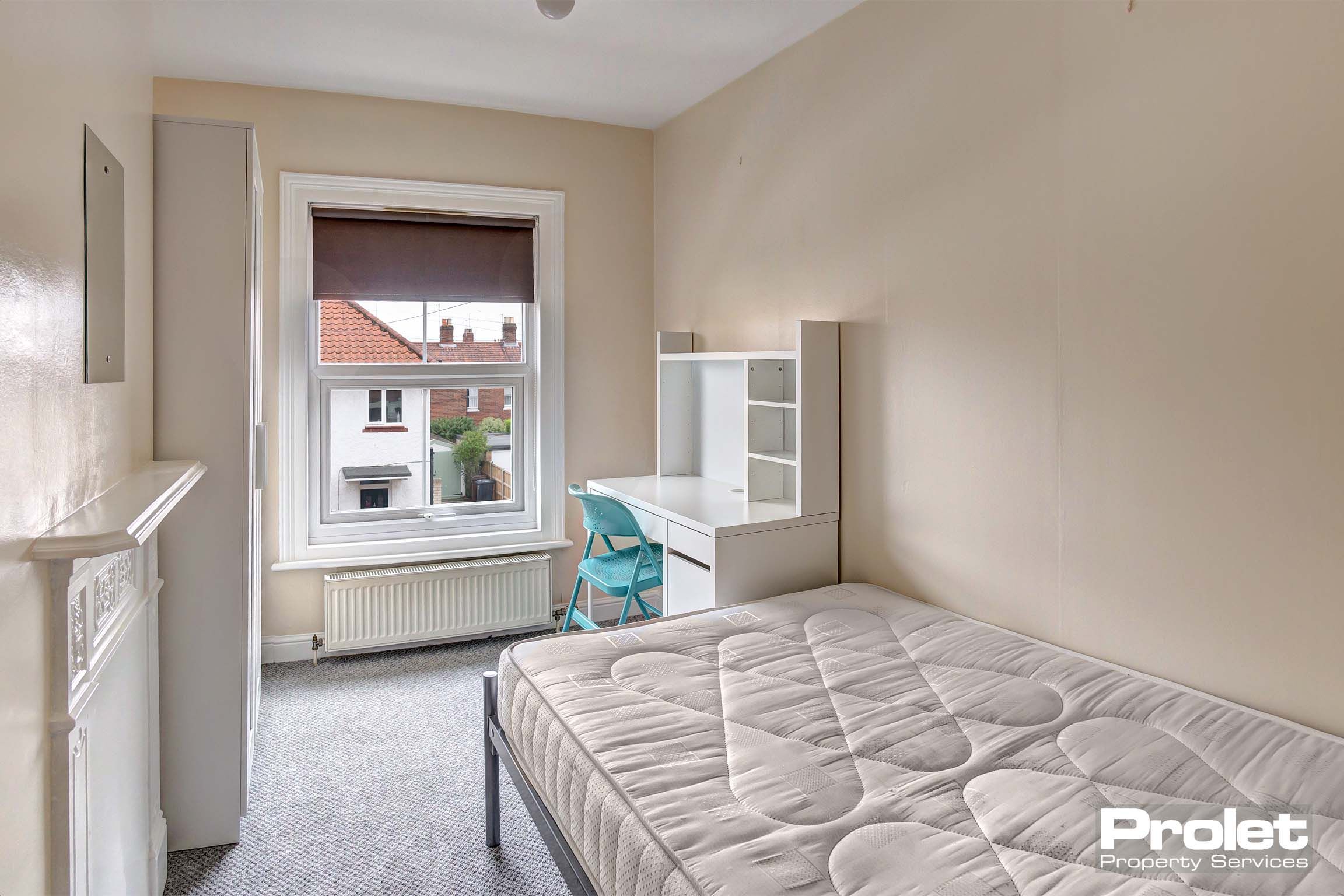 Double bedroom with magnolia painted walls with white wardrobe and a desk. A decorative fireplace.