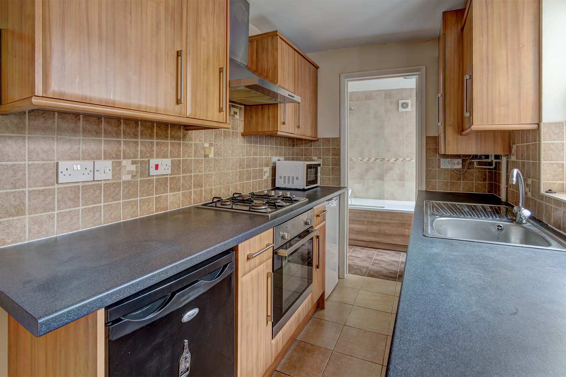 Wooden fitted kitchen with black work tops. An oven and hob with extractor fan. A silver sink and tap and a white fridge/freezer.