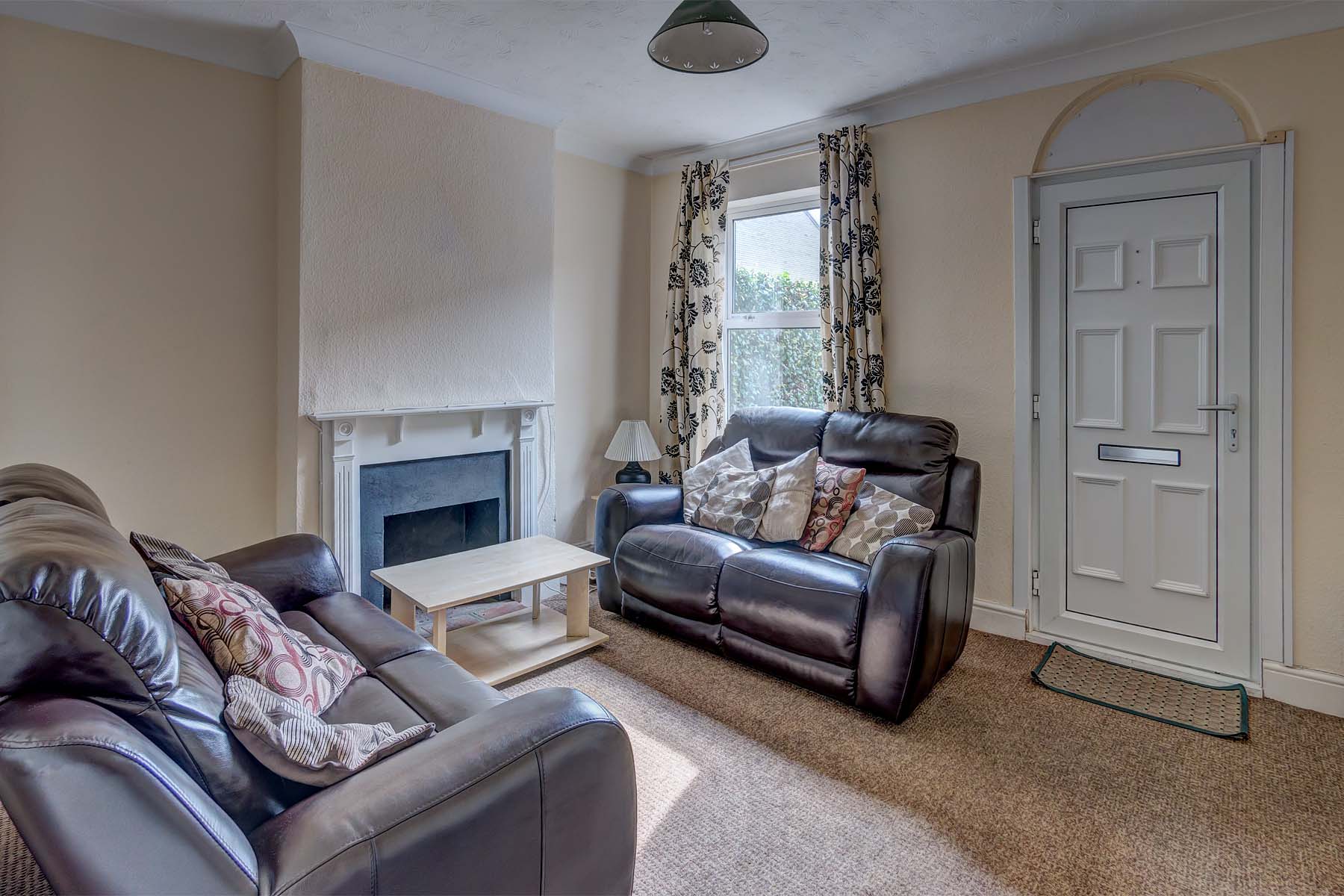 Lounge area with two black leather sofas, a coffee table and decorative fireplace. Front door entry.