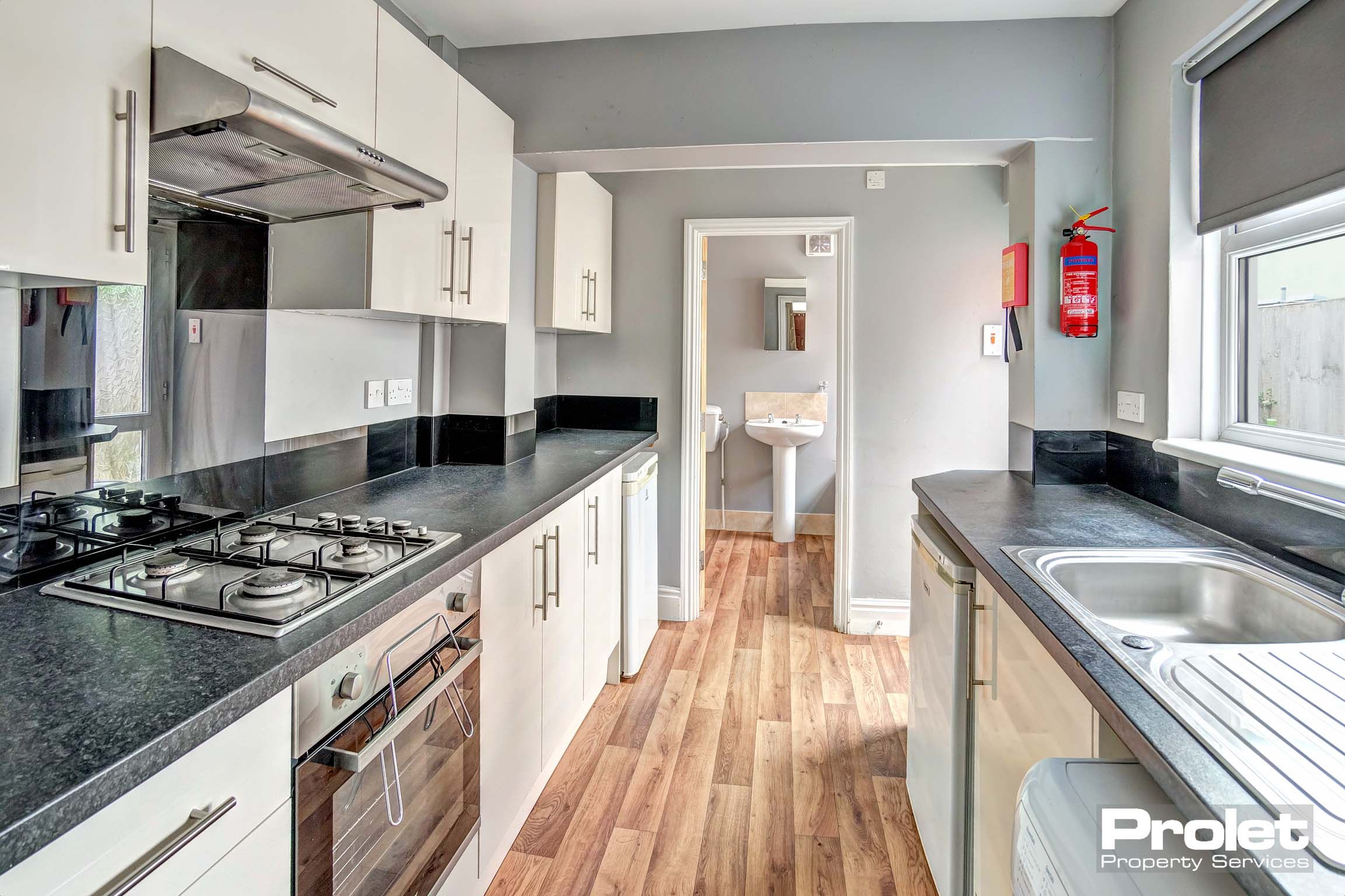 Galley kitchen with wood effect flooring, white cabinets, and black worktop.