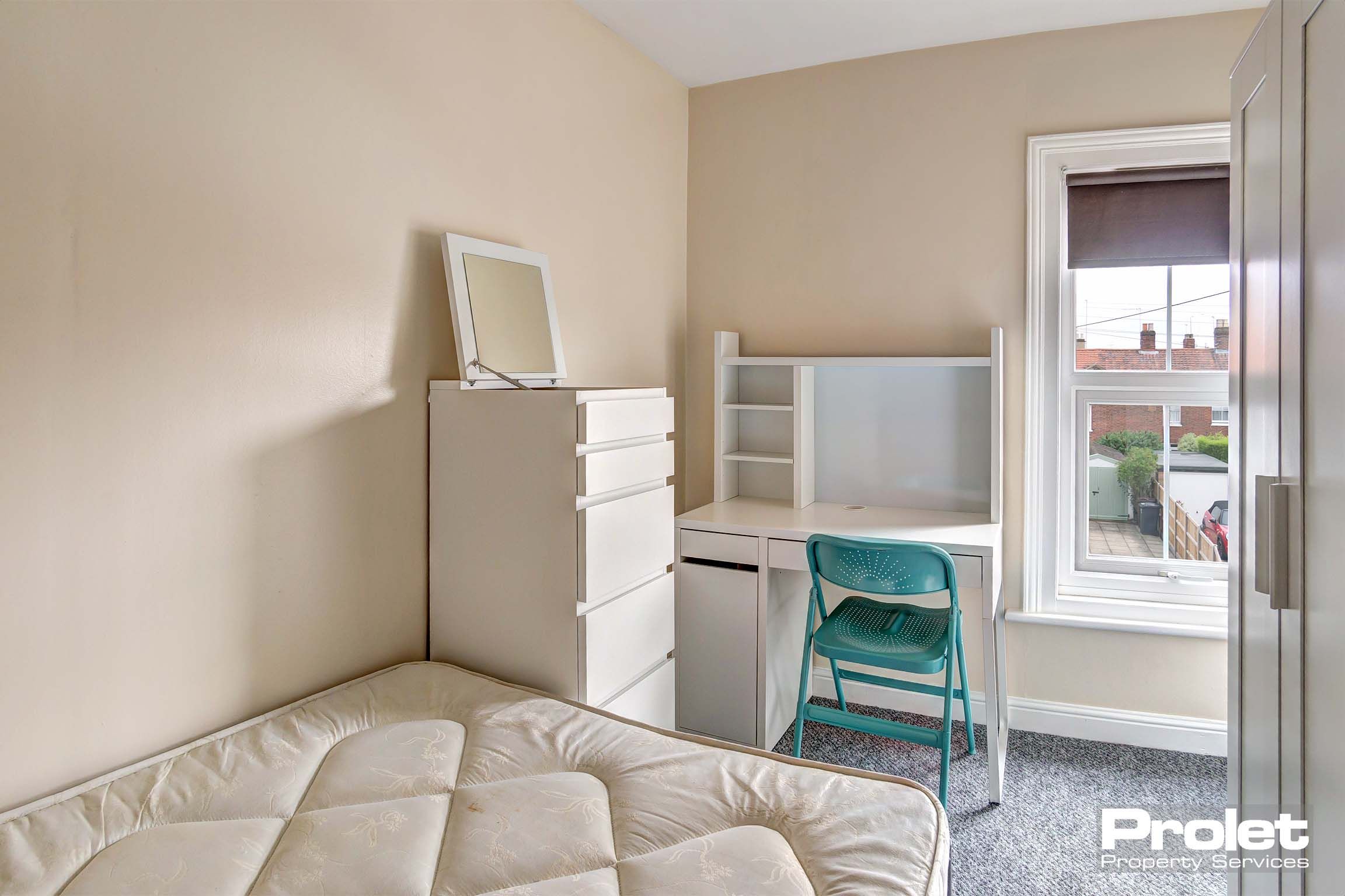 Double bedroom with magnolia walls. White wardrobe with matching desk and tall chest of drawers.